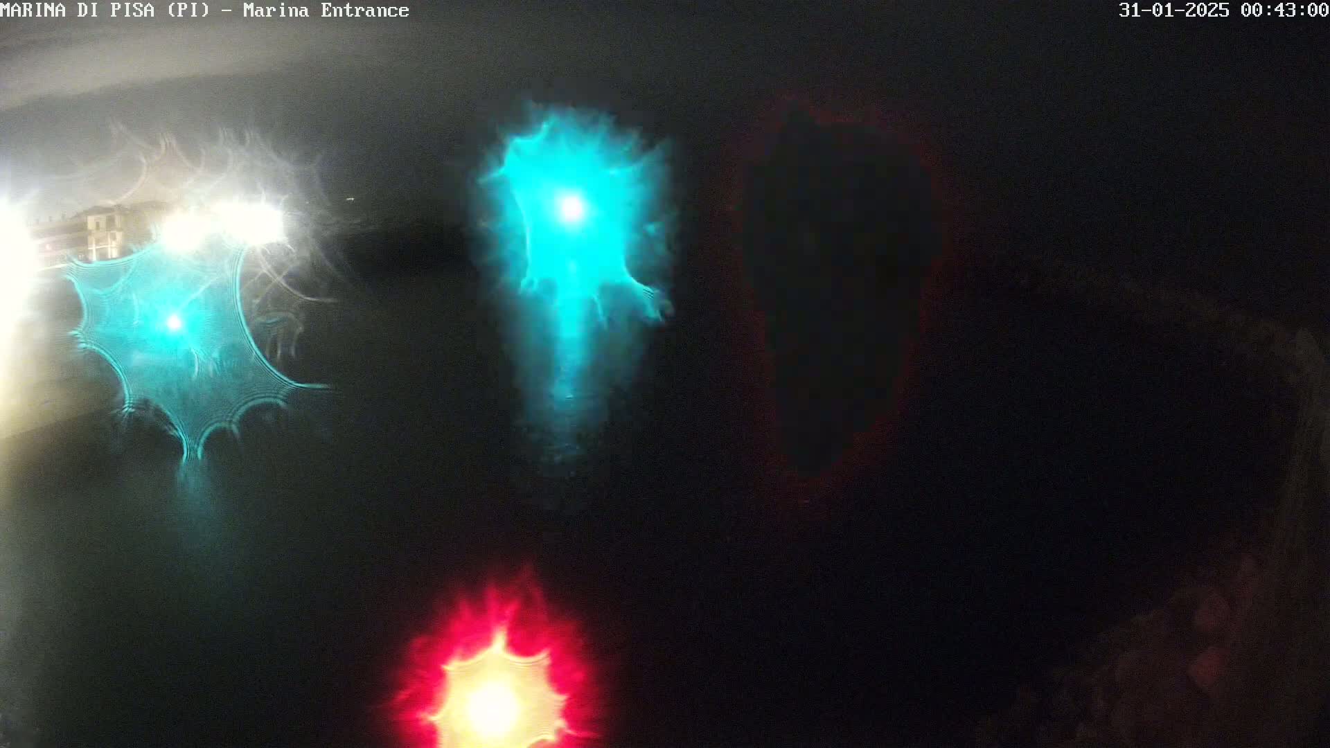 A nighttime, blurry image shows distorted reflections of teal and red lights on dark water.