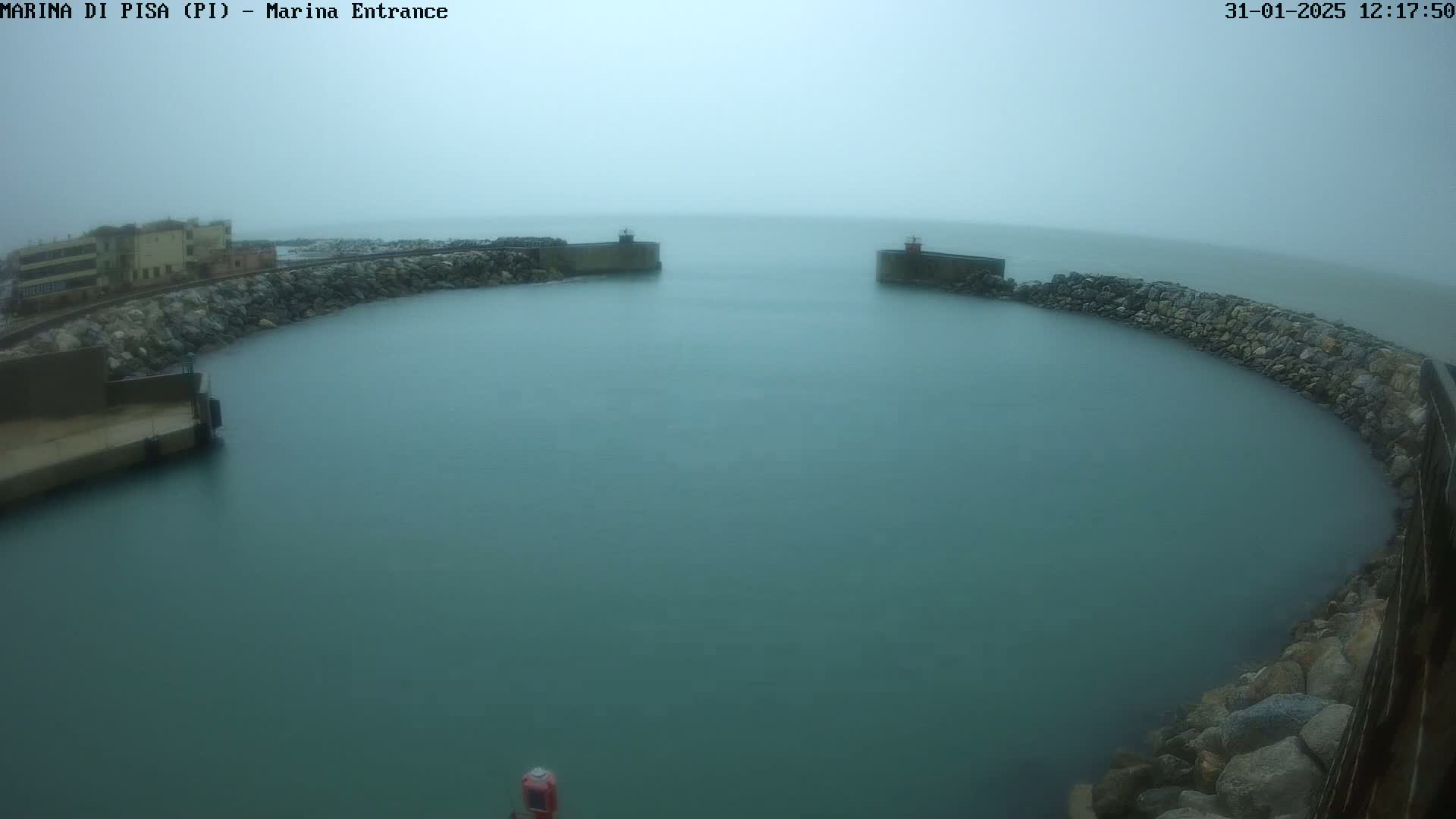 A calm, teal-colored harbor is enclosed by a curved stone wall under an overcast sky.