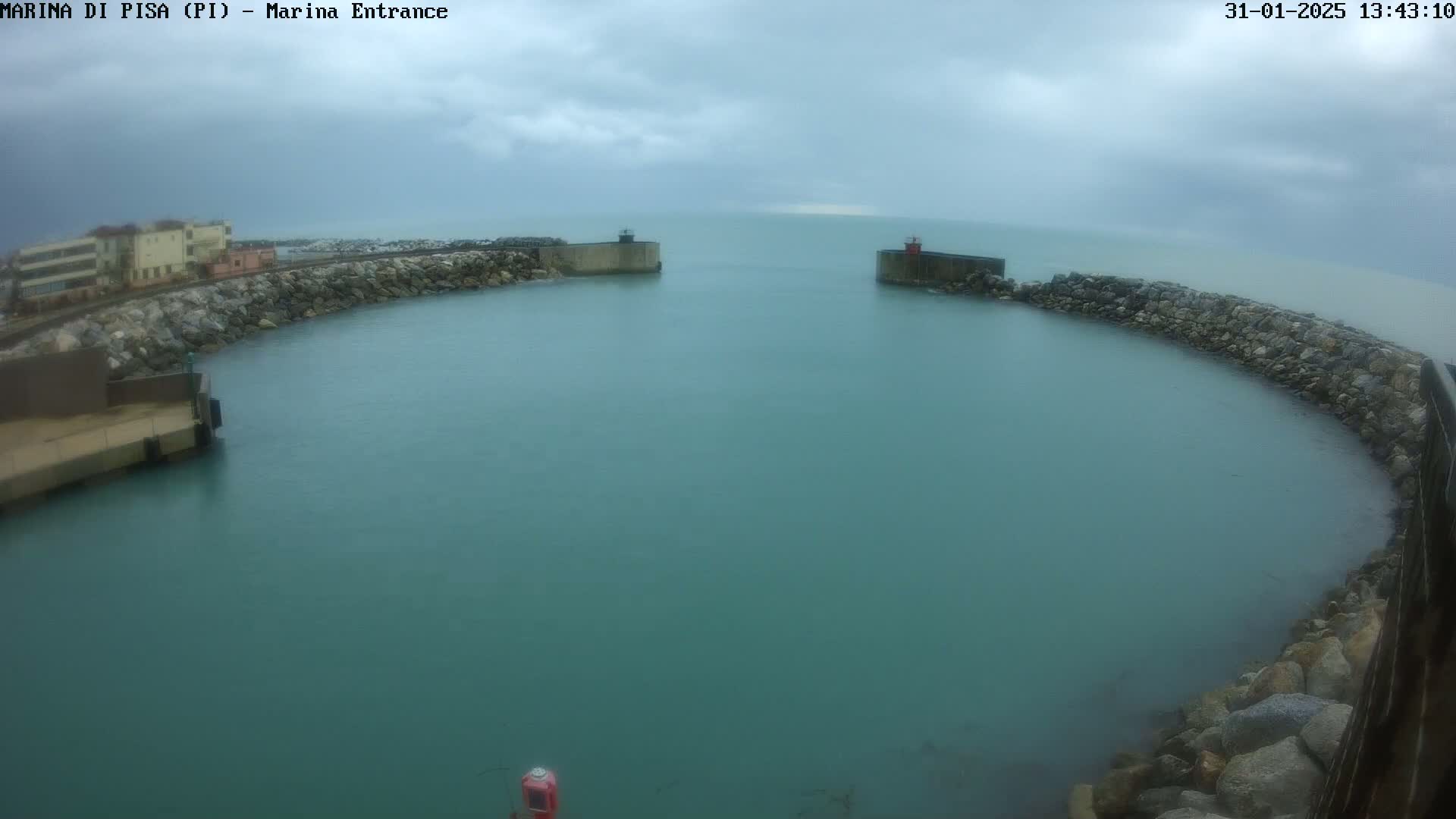 A harbor entrance with calm, teal water is enclosed by rock walls under an overcast sky.