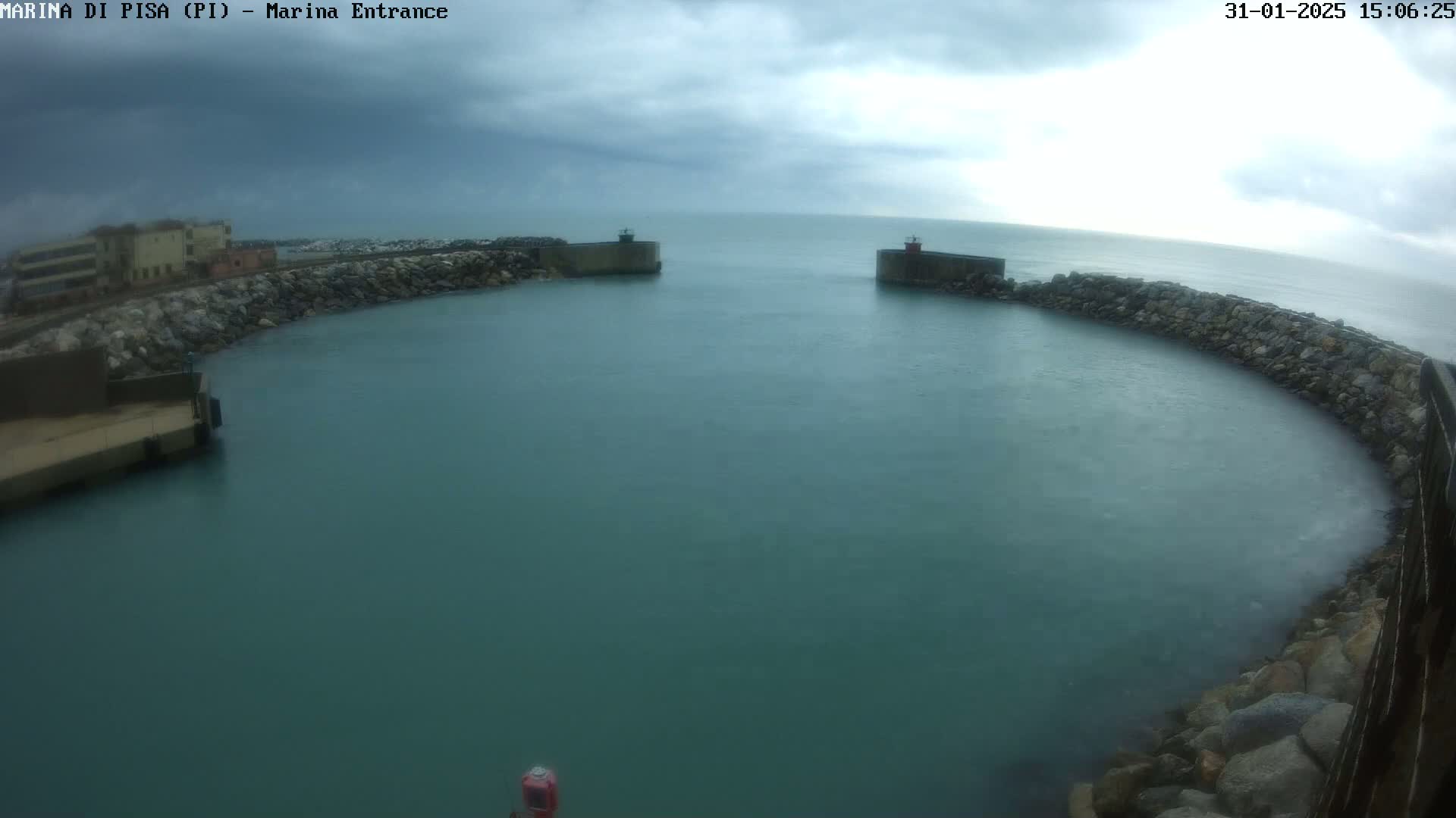 A harbor entrance with calm, teal water is partially enclosed by stone walls under an overcast sky.