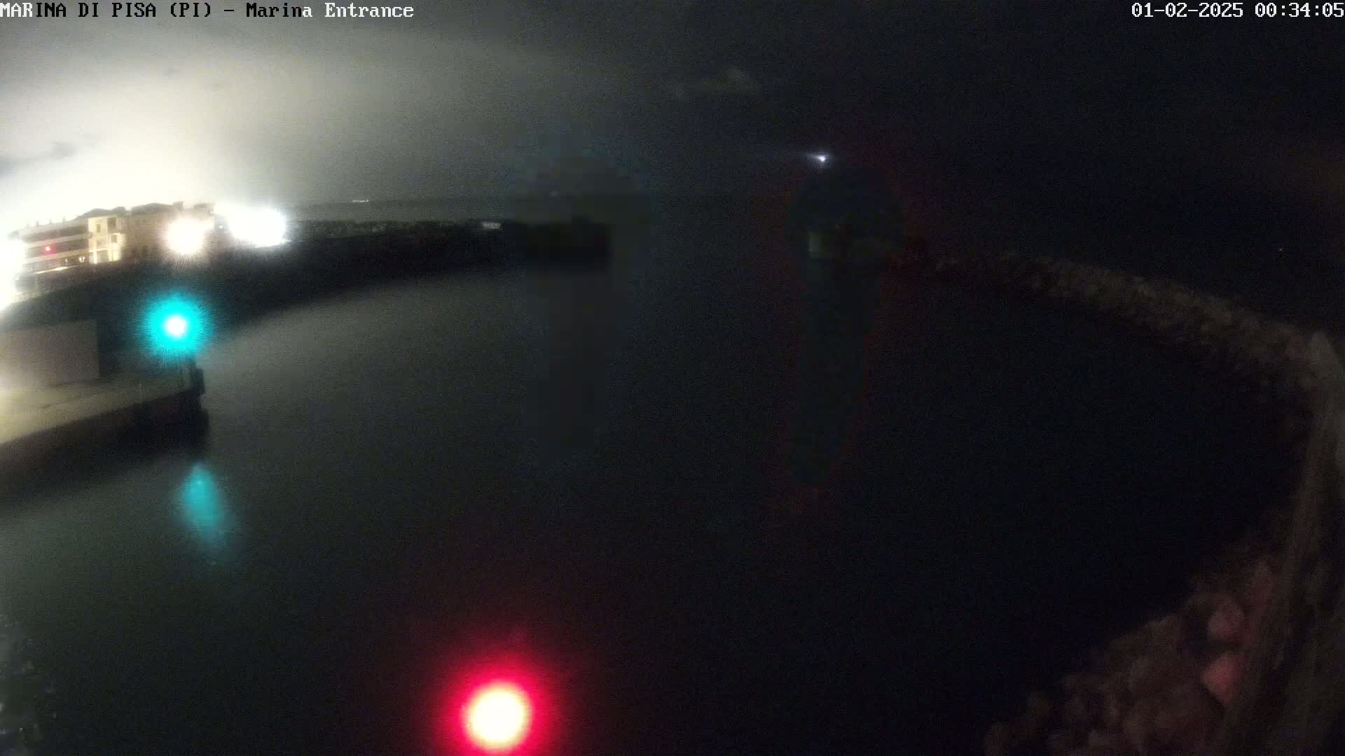 A nighttime view of a dark body of water with a building and lights visible on the shore under a cloudy sky.