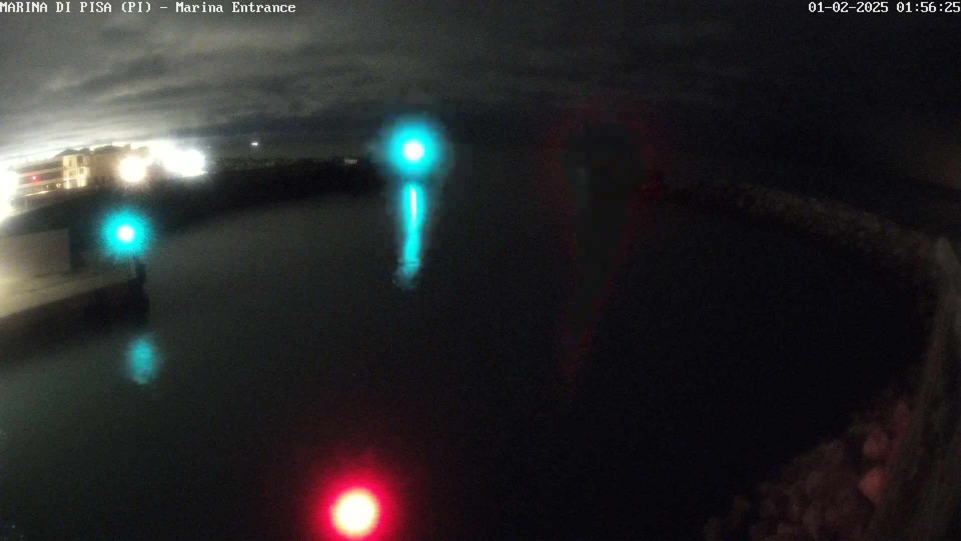 A nighttime, overcast view of a dark body of water with illuminated navigation lights and a building faintly visible in the background.