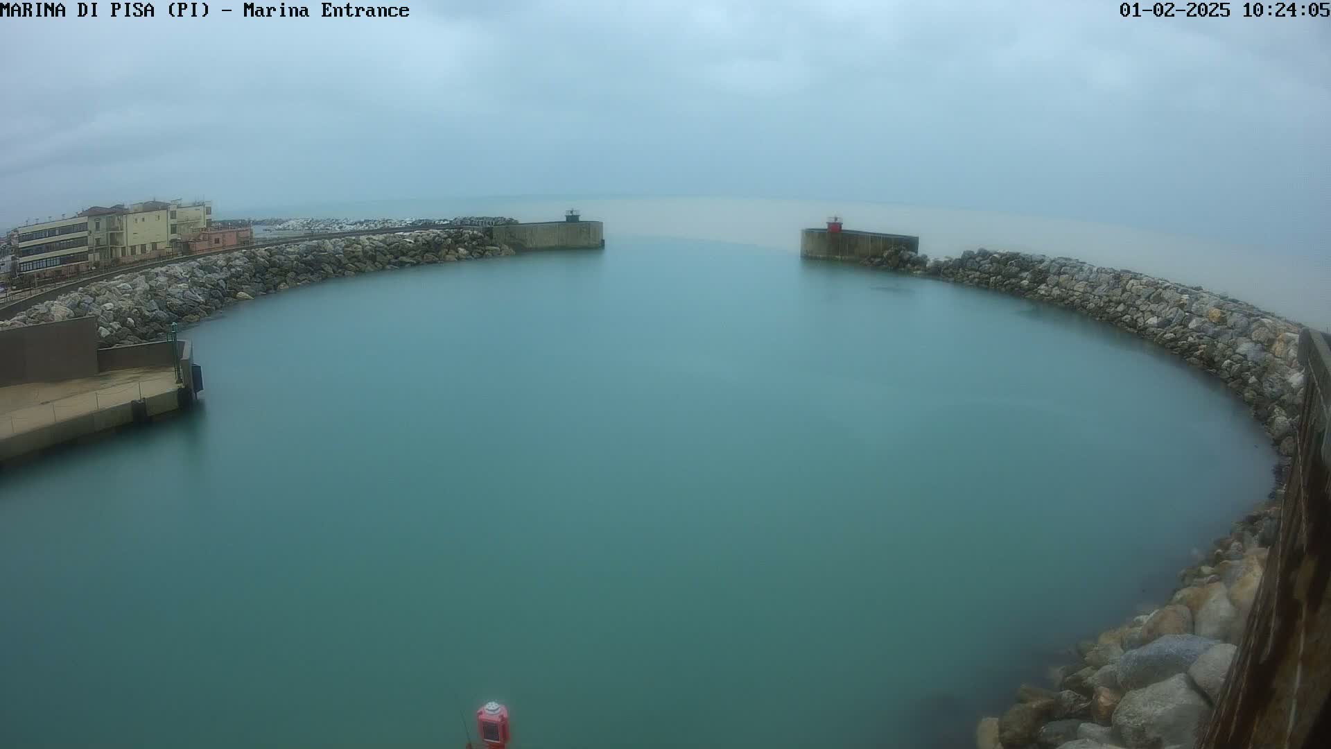 A calm, teal-colored harbor is enclosed by stone walls under an overcast sky.