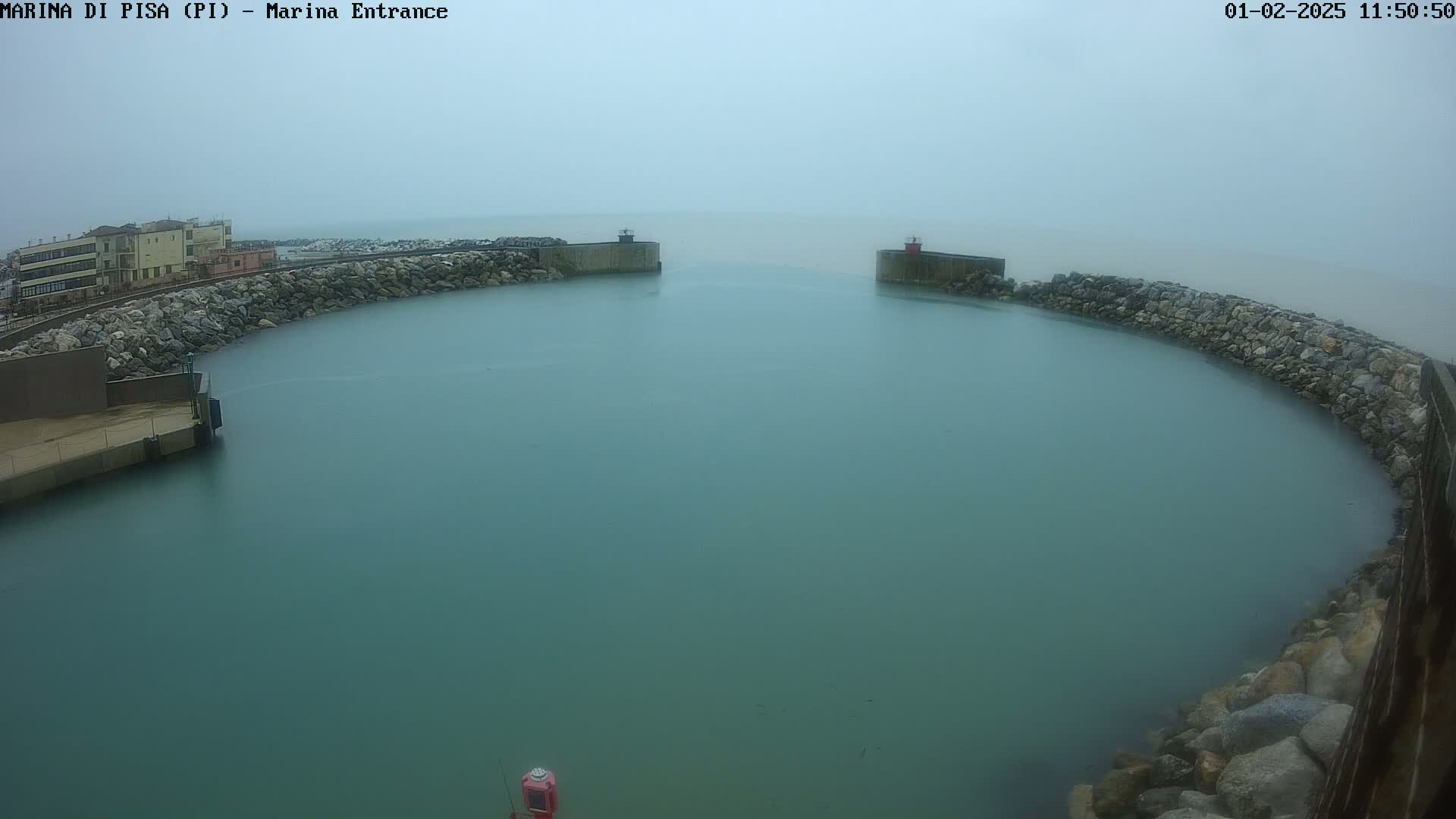 A calm, teal-colored harbor is partially enclosed by rock walls under a foggy sky.