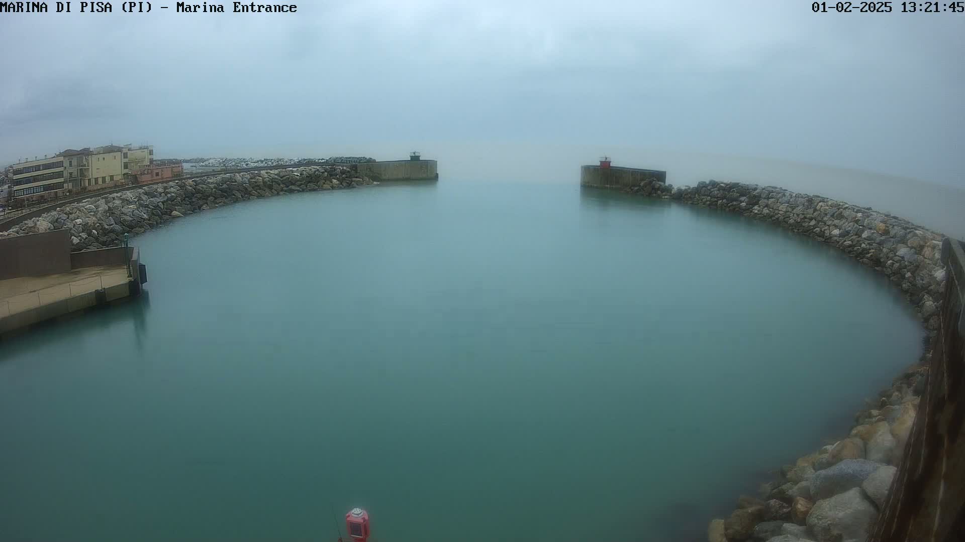 A calm, teal harbor is enclosed by rock walls on an overcast day.
