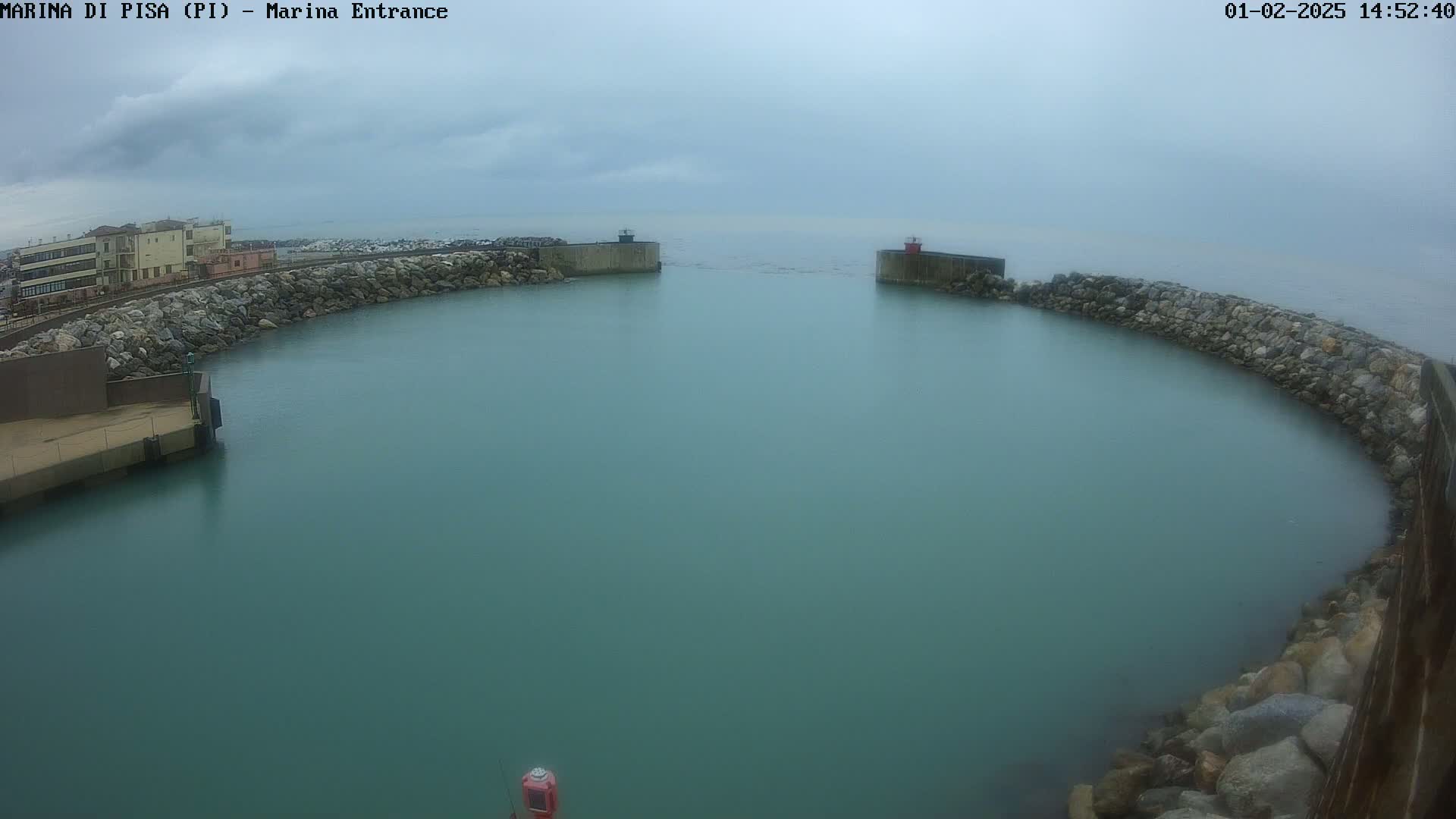 A calm, overcast day shows a harbor entrance bordered by rock walls and a building in the distance.