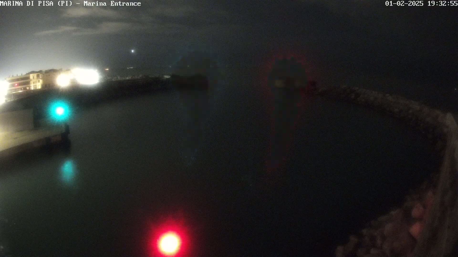 A nighttime view of a dark harbor with faint lights reflecting on the water, illuminated by building lights on the shore and navigational lights in the water.
