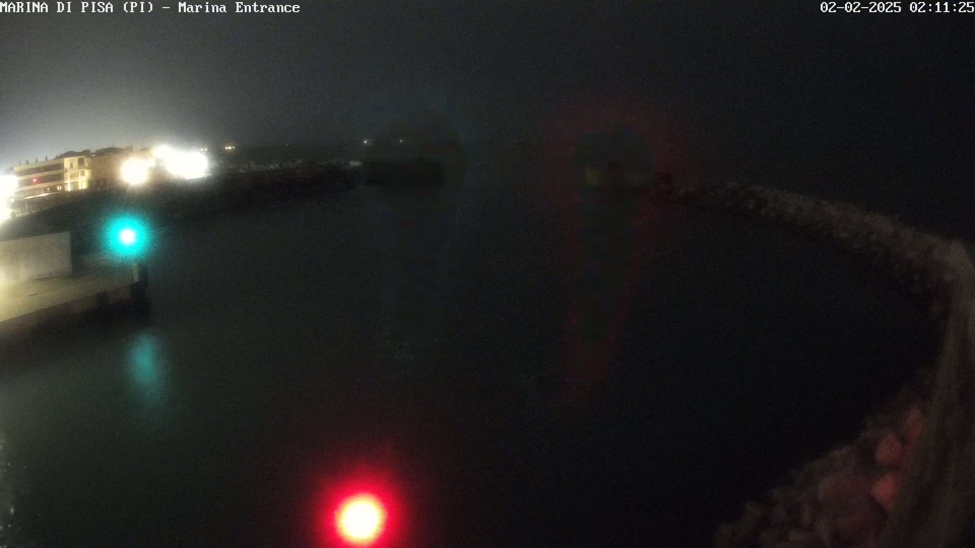 A nighttime, foggy view of a dark harbor with a few lights visible on the shore and in the water.