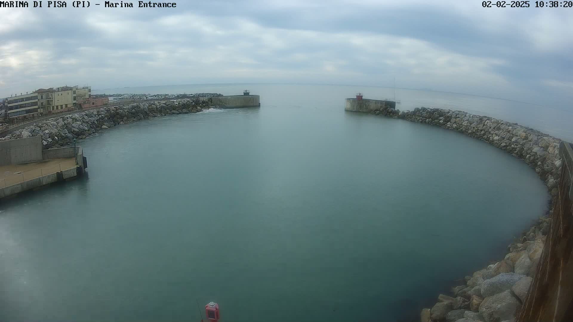 A calm, overcast day shows a harbor entrance with two concrete breakwaters curving into a tranquil body of teal water.