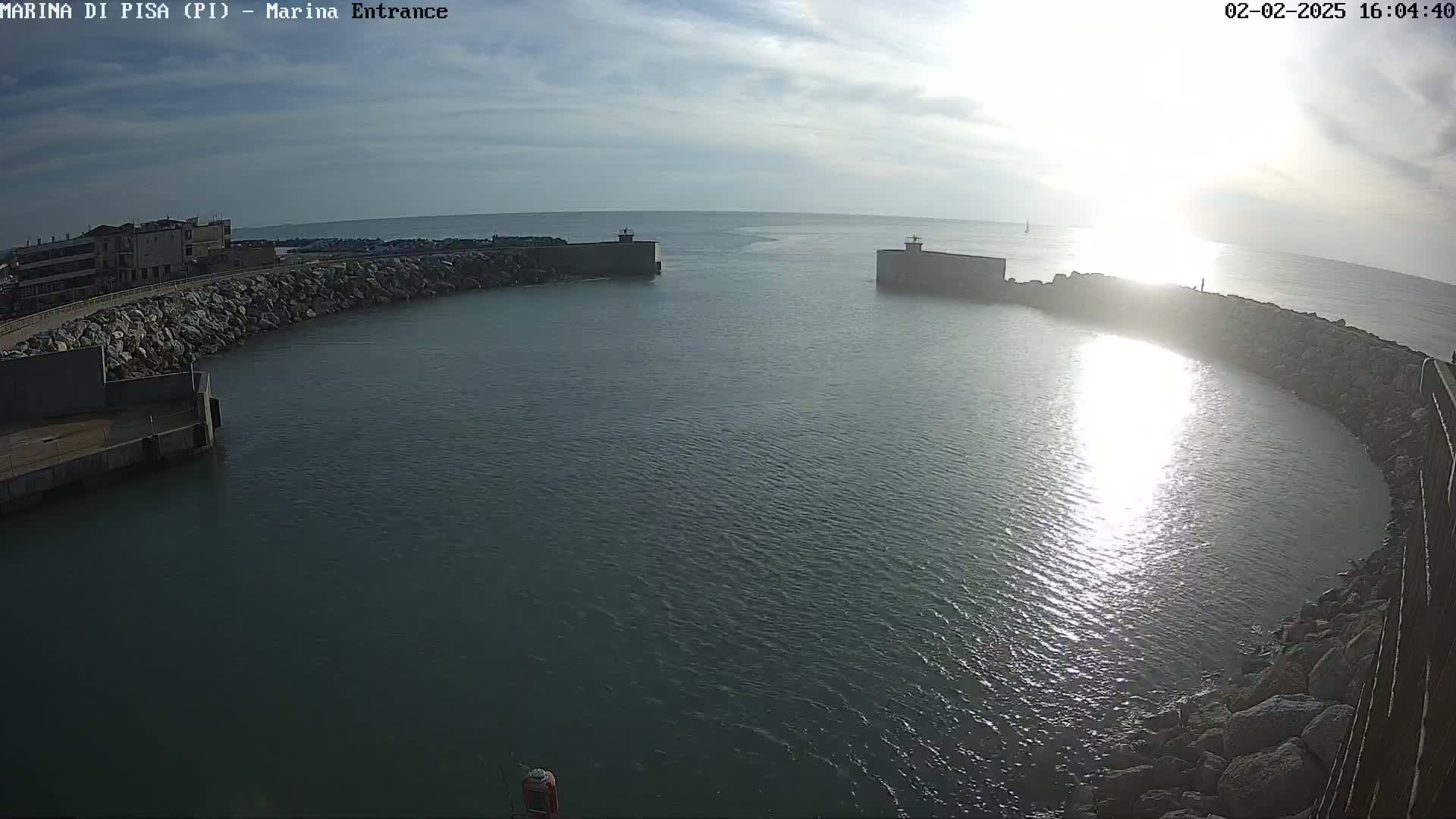 A harbor entrance with calm water reflecting sunlight under a partly cloudy sky.