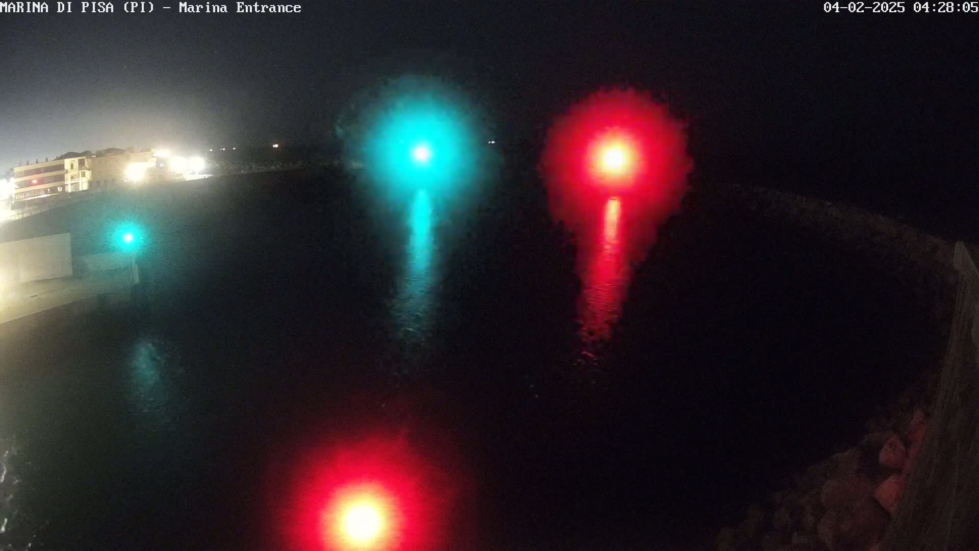 At night, three bright lights—one teal and two red—illuminate dark water reflecting their glow.