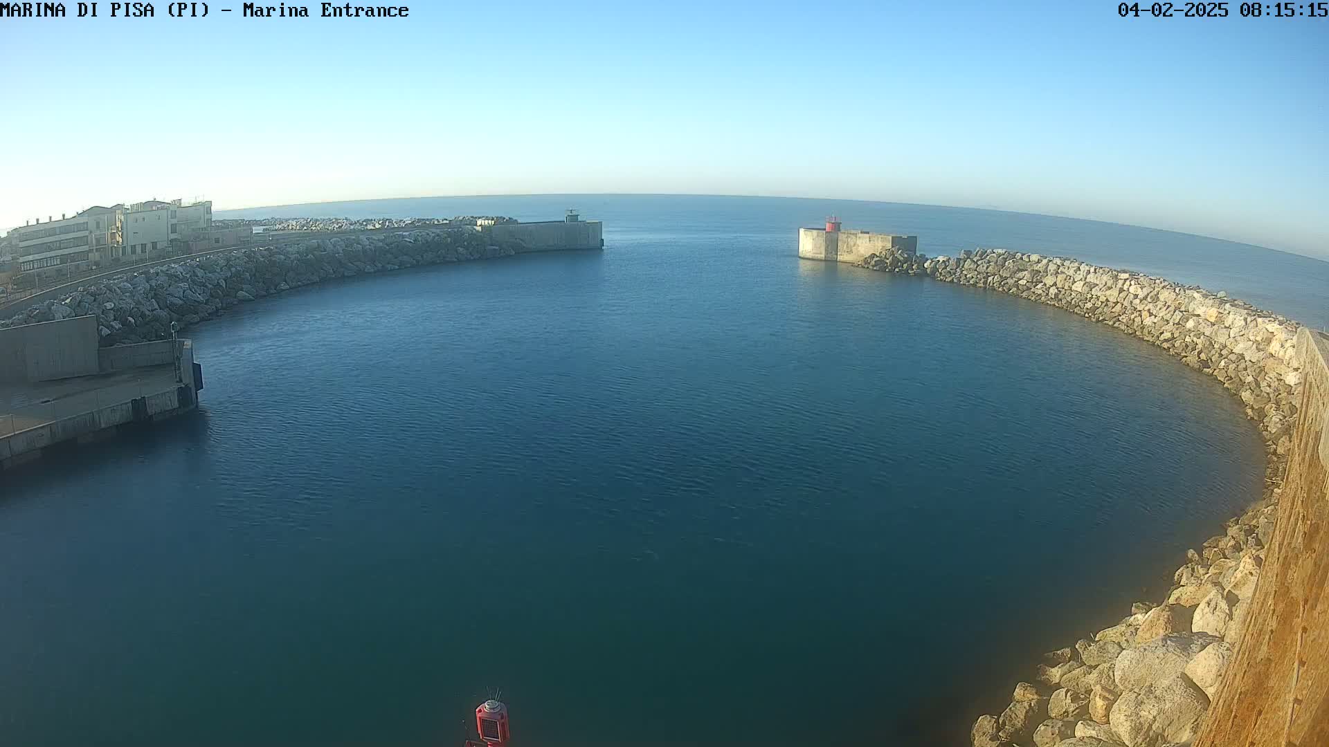 A harbor entrance with calm, blue water is seen from an elevated viewpoint under a clear sky.