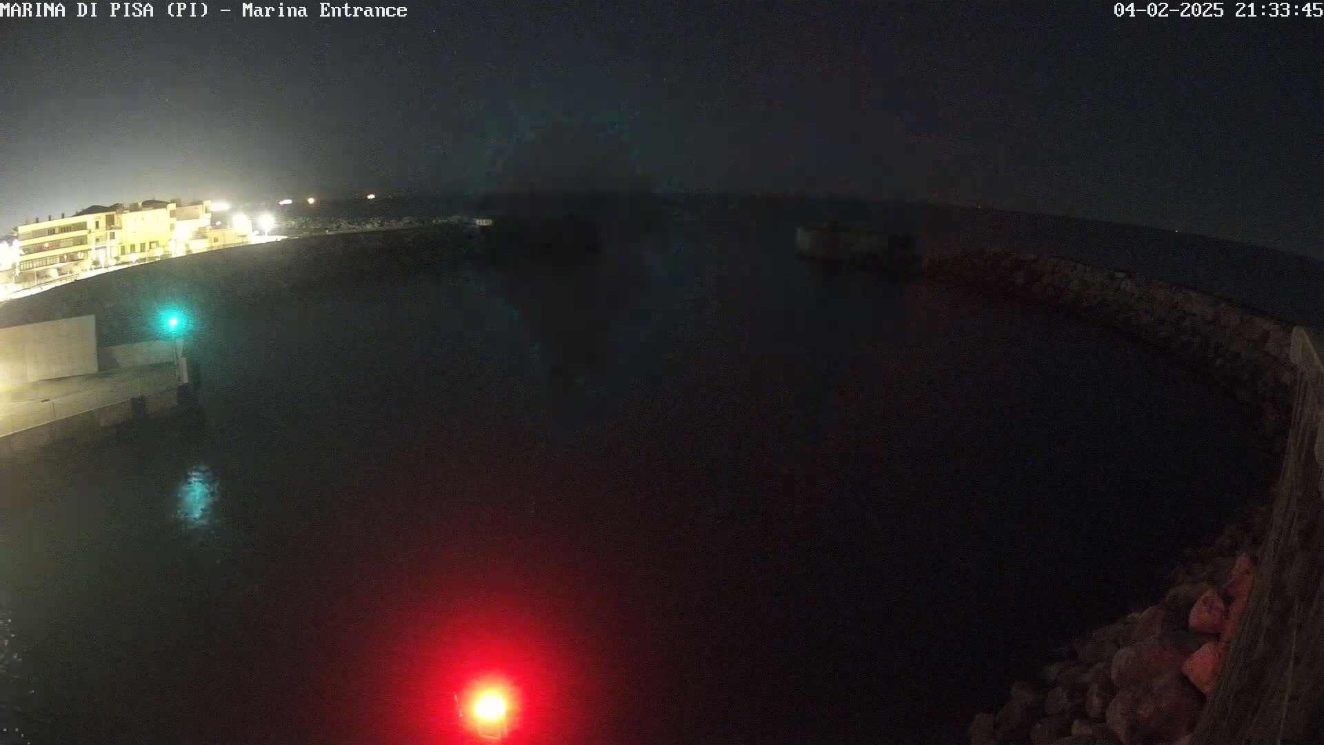 A nighttime, dark view of a harbor entrance with a building and low light levels, showing calm water.