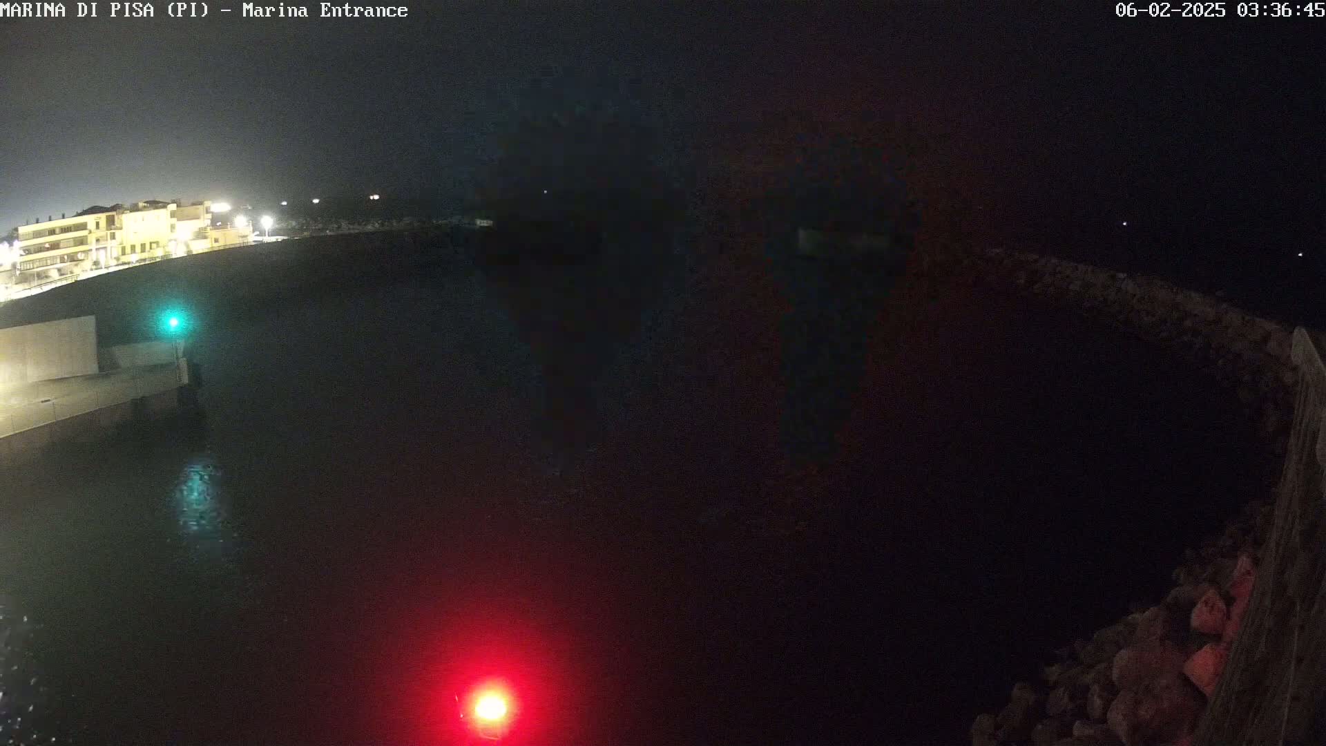 A nighttime view of a dark body of water next to a lit-up building and a rocky shoreline, under a clear, dark sky.