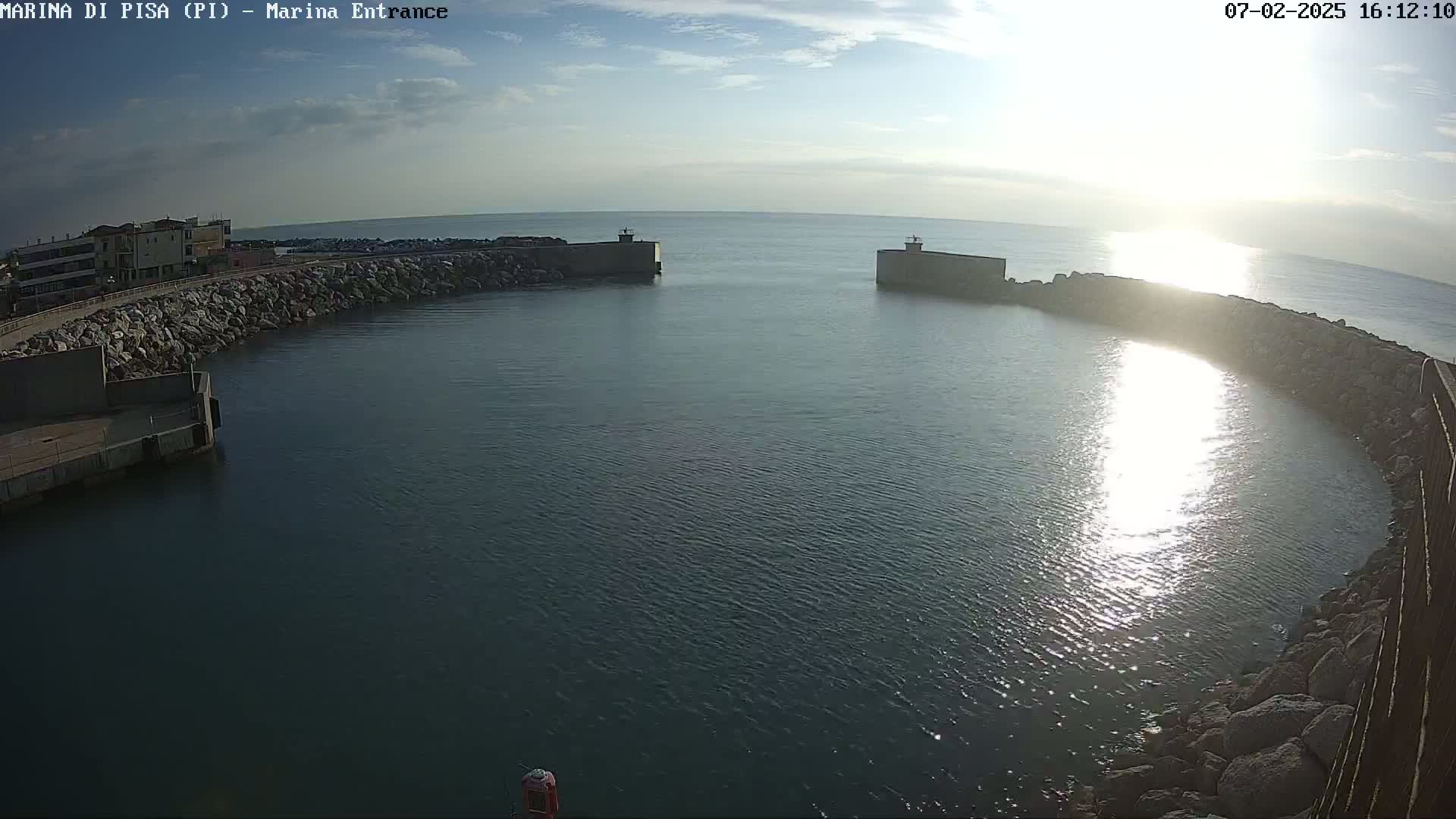 A harbor entrance with calm water reflecting sunlight under a mostly clear sky.