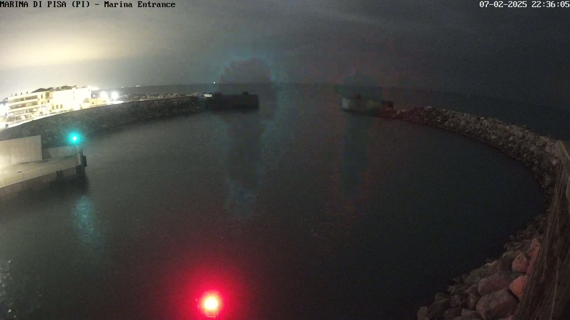 A nighttime view of a calm harbor enclosed by a curved stone wall, under an overcast sky.