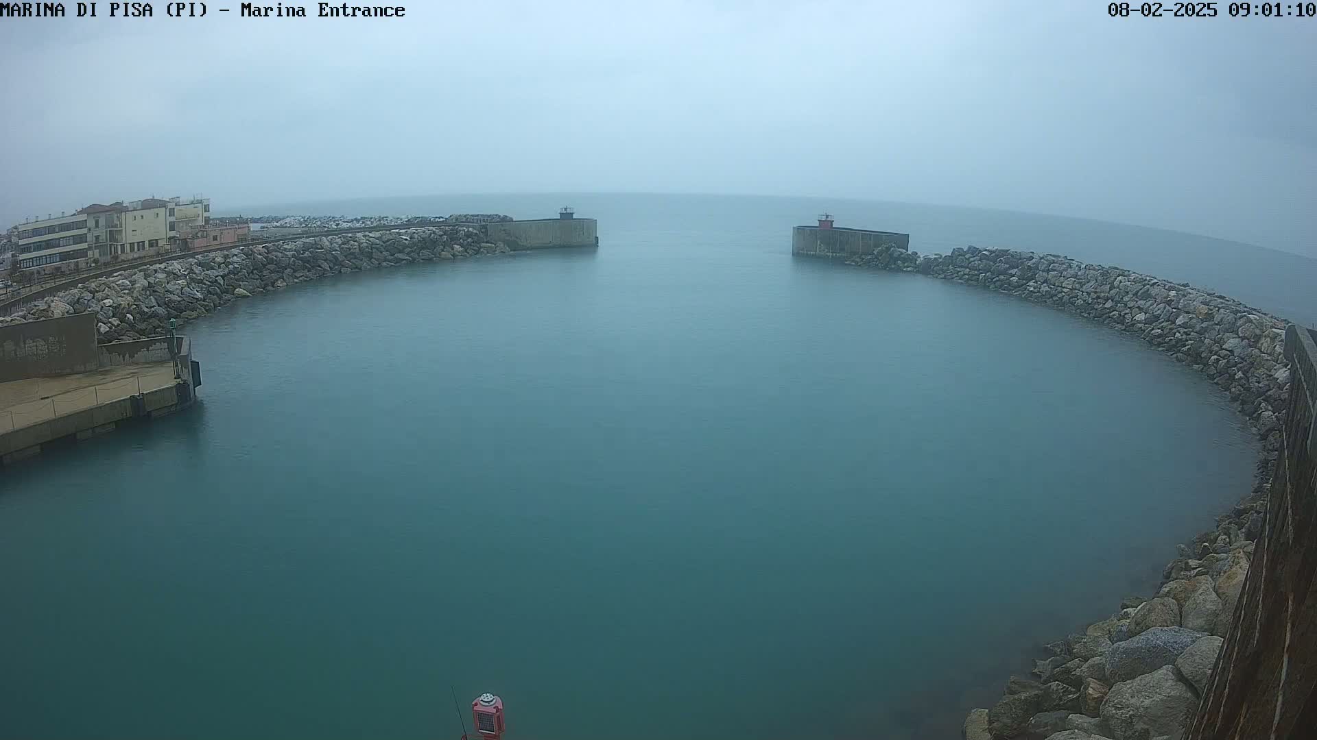 A calm, hazy harbor entrance is seen from an elevated position, with a building visible in the distance to one side.