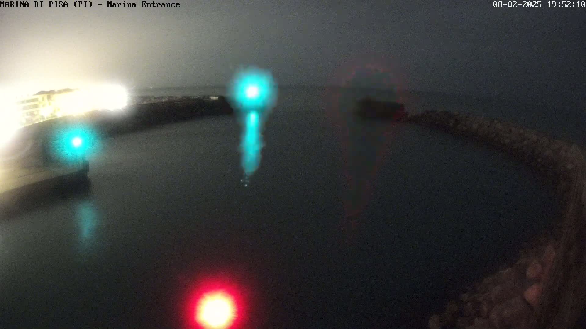 A nighttime view of a dark body of water with brightly lit structures on either side, illuminated by a teal light and a red light.