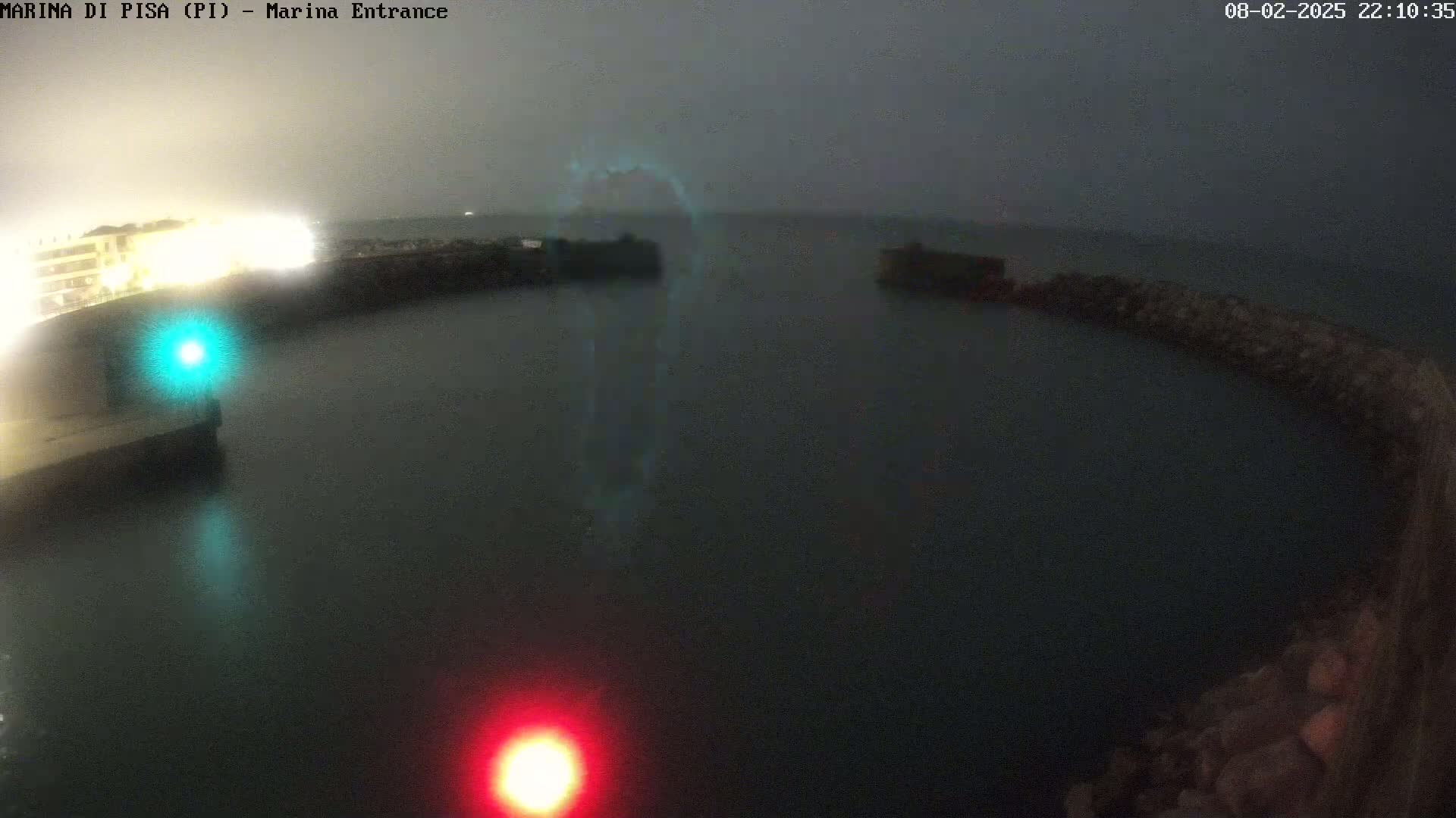 A nighttime view of a dark, calm harbor with lights on the docks under an overcast sky.