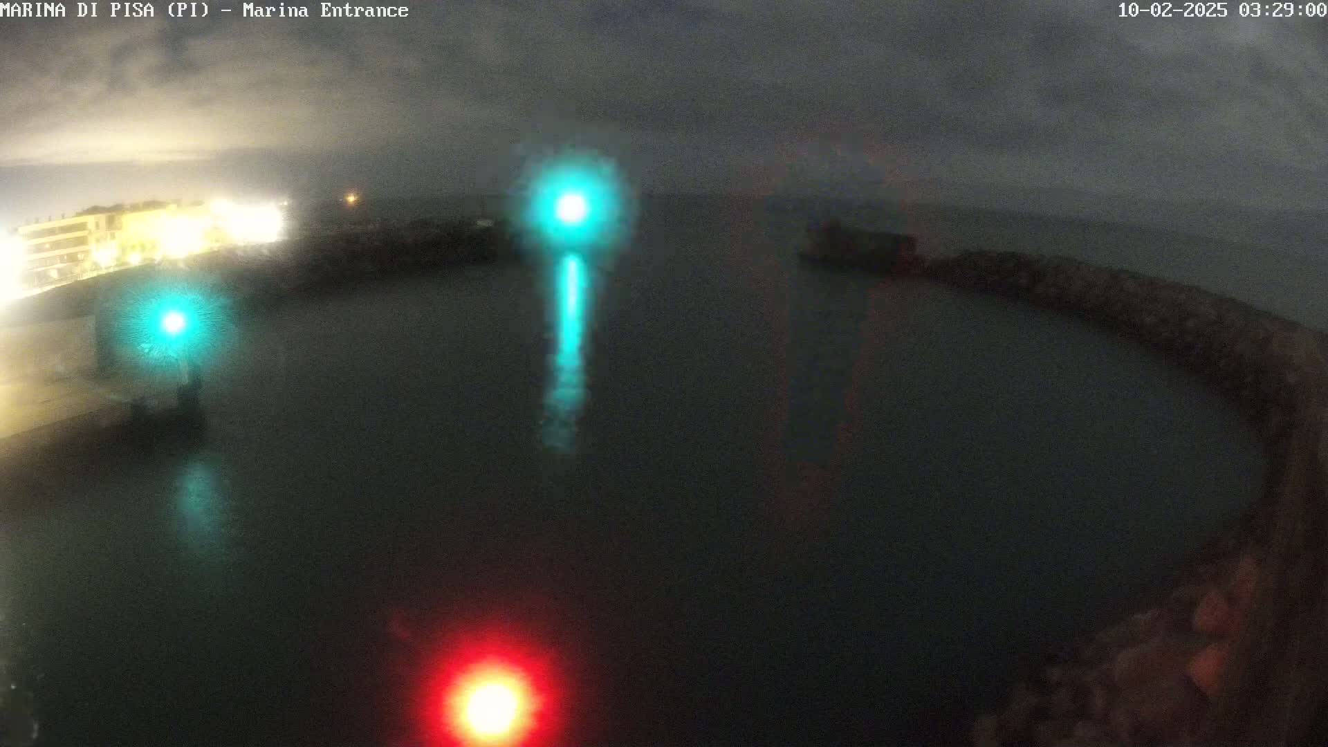A nighttime view of a harbor entrance with calm water, illuminated by a green and a red light.