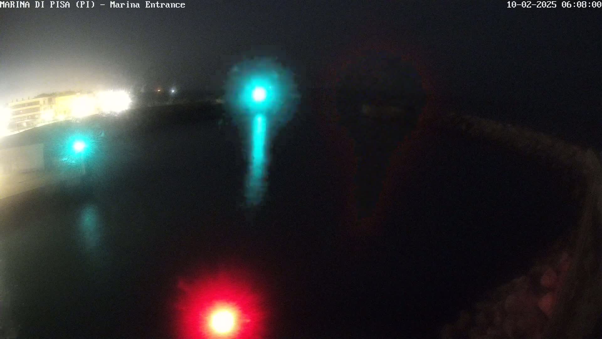 At night, a dark body of water reflects bright green and red lights from a distance, with a hazy or foggy atmosphere.