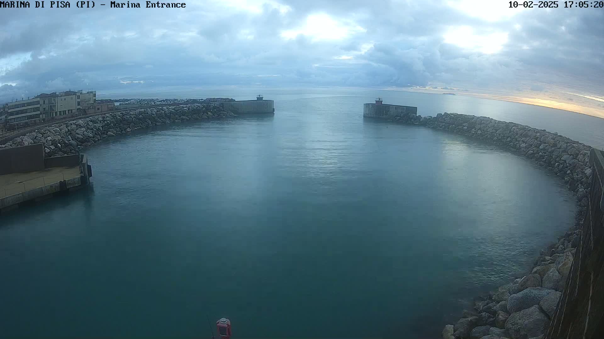 A calm harbor entrance with cloudy skies is partially enclosed by stone walls.