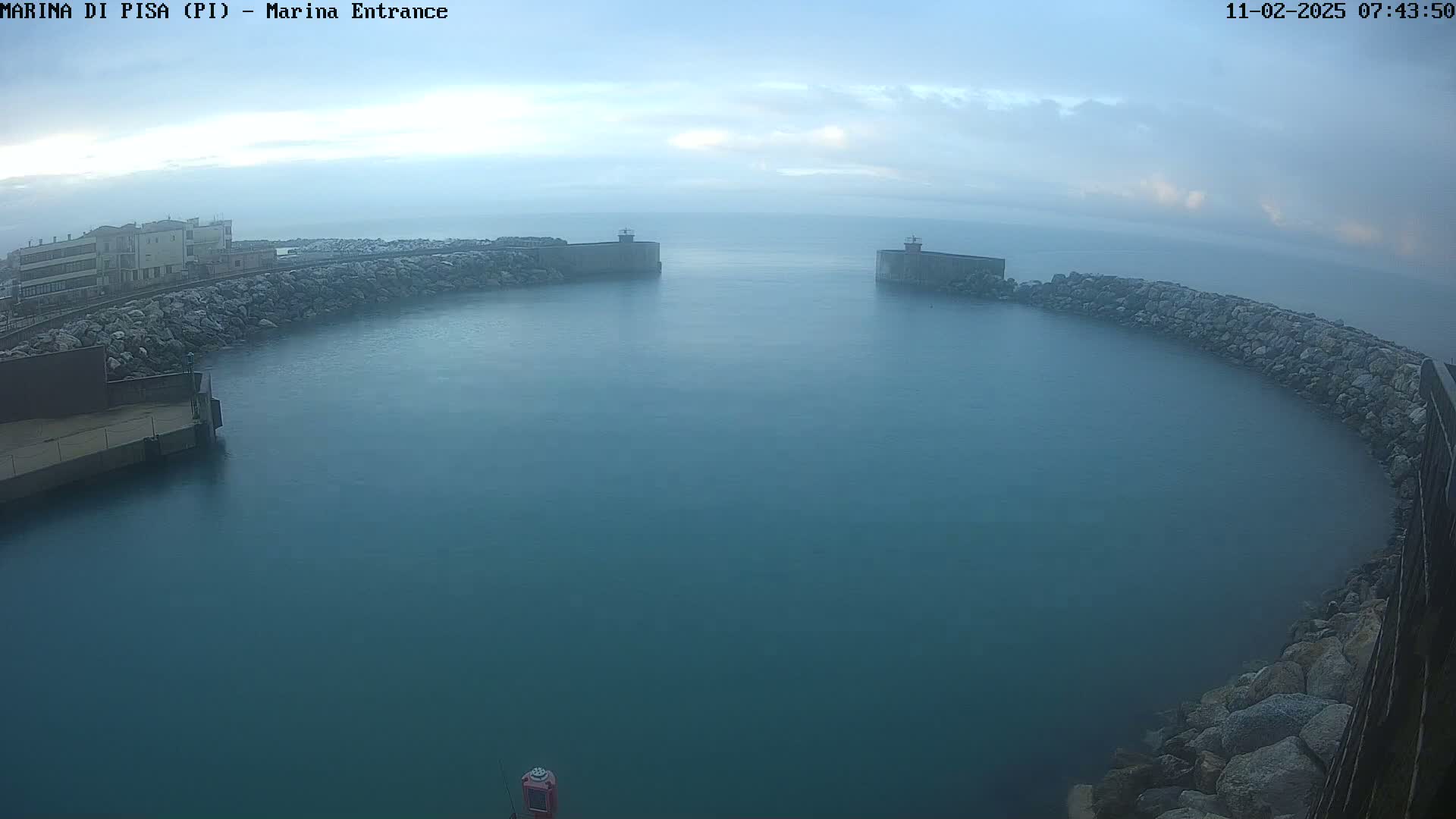 A calm, misty harbor is seen from an elevated vantage point, with stone walls forming a curved entrance to a body of dark teal water.