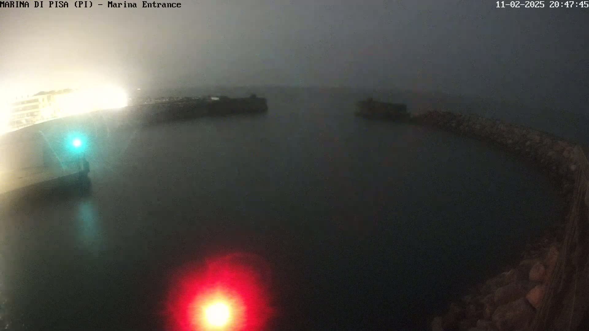 A foggy night scene shows a dark body of water enclosed by stone walls with a red and green light visible.