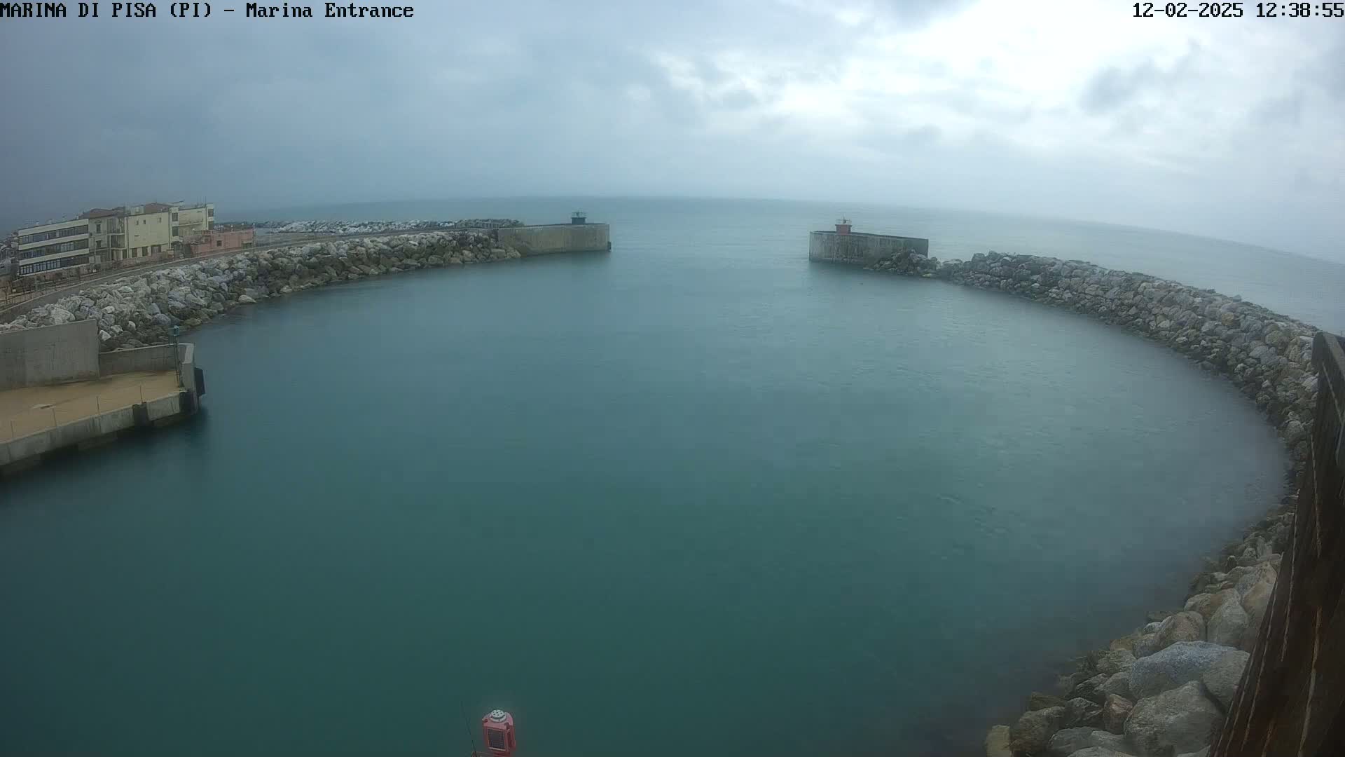 A harbor entrance with calm, dark-green water is partially enclosed by rock walls on an overcast day.