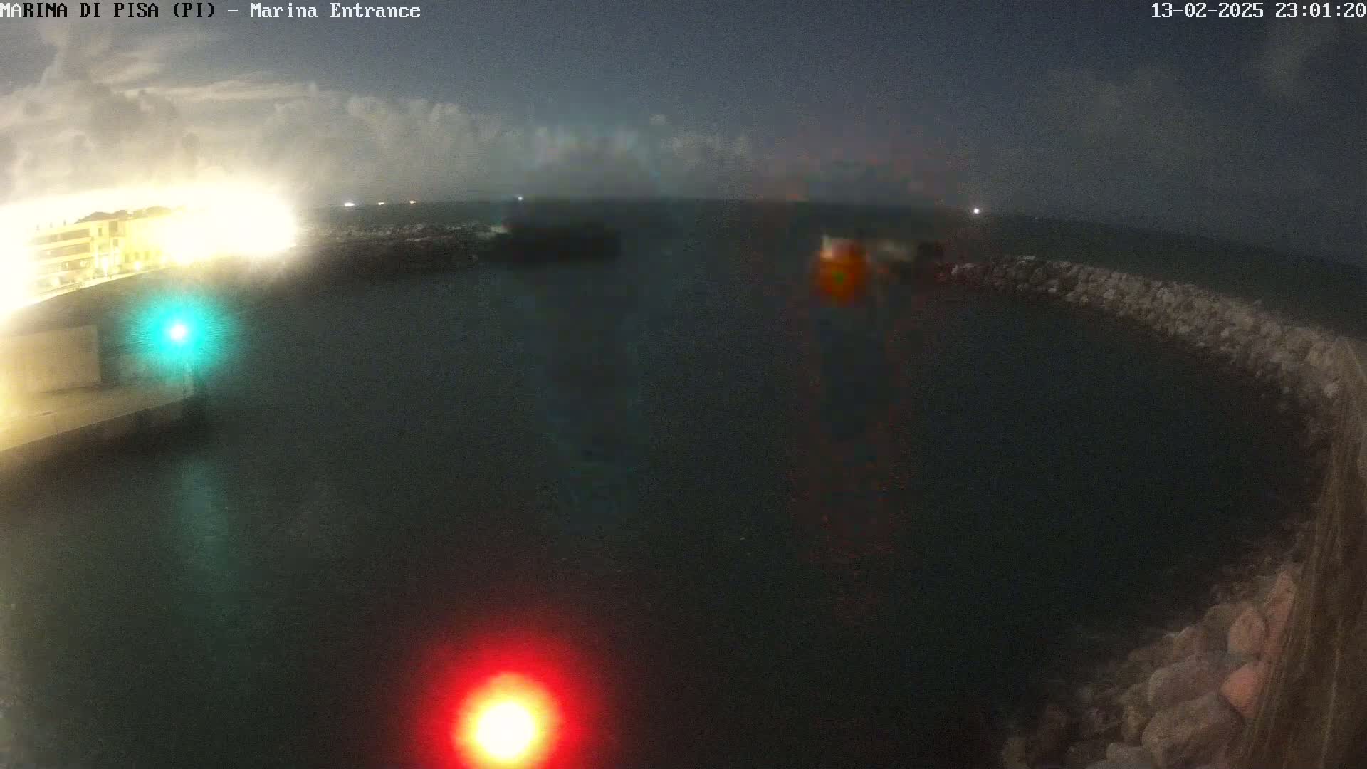 A nighttime view of a dark harbor with a partially visible building and breakwater, under a cloudy sky.