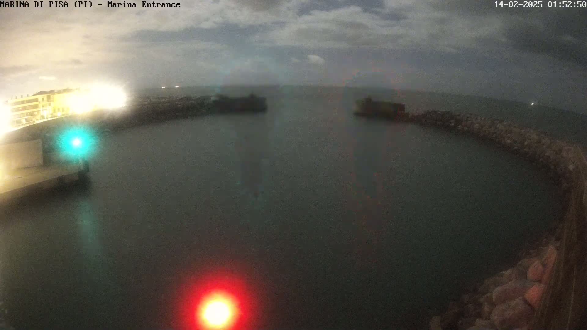 A nighttime view of a harbor entrance with calm water, showing a dark sky with some clouds.