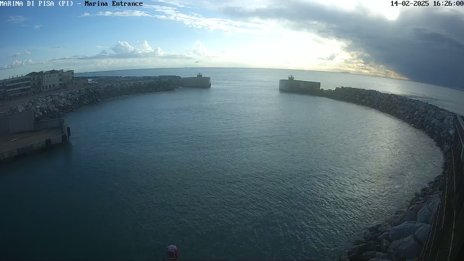 A harbor entrance with calm water under a partly cloudy sky is seen from an aerial view.