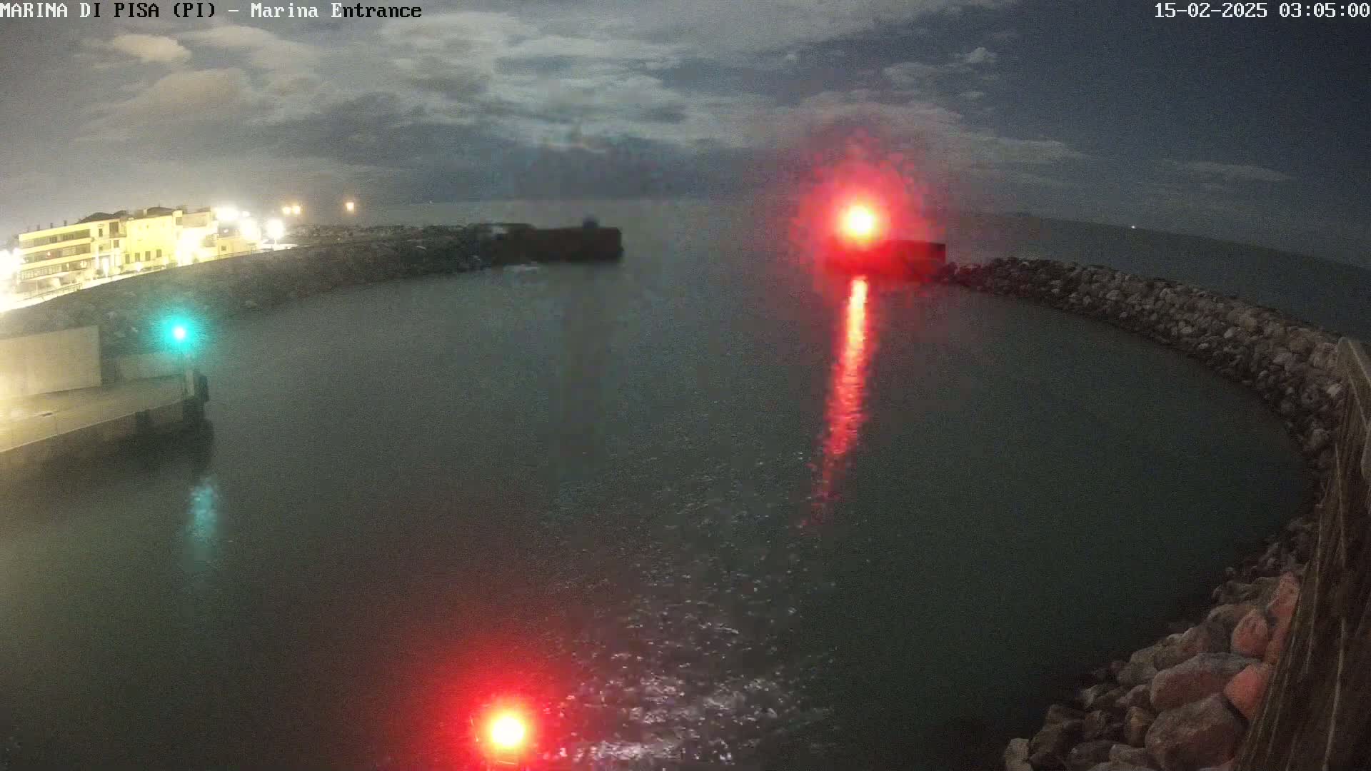 A nighttime view of a harbor entrance with red and green navigational lights, under a cloudy sky.