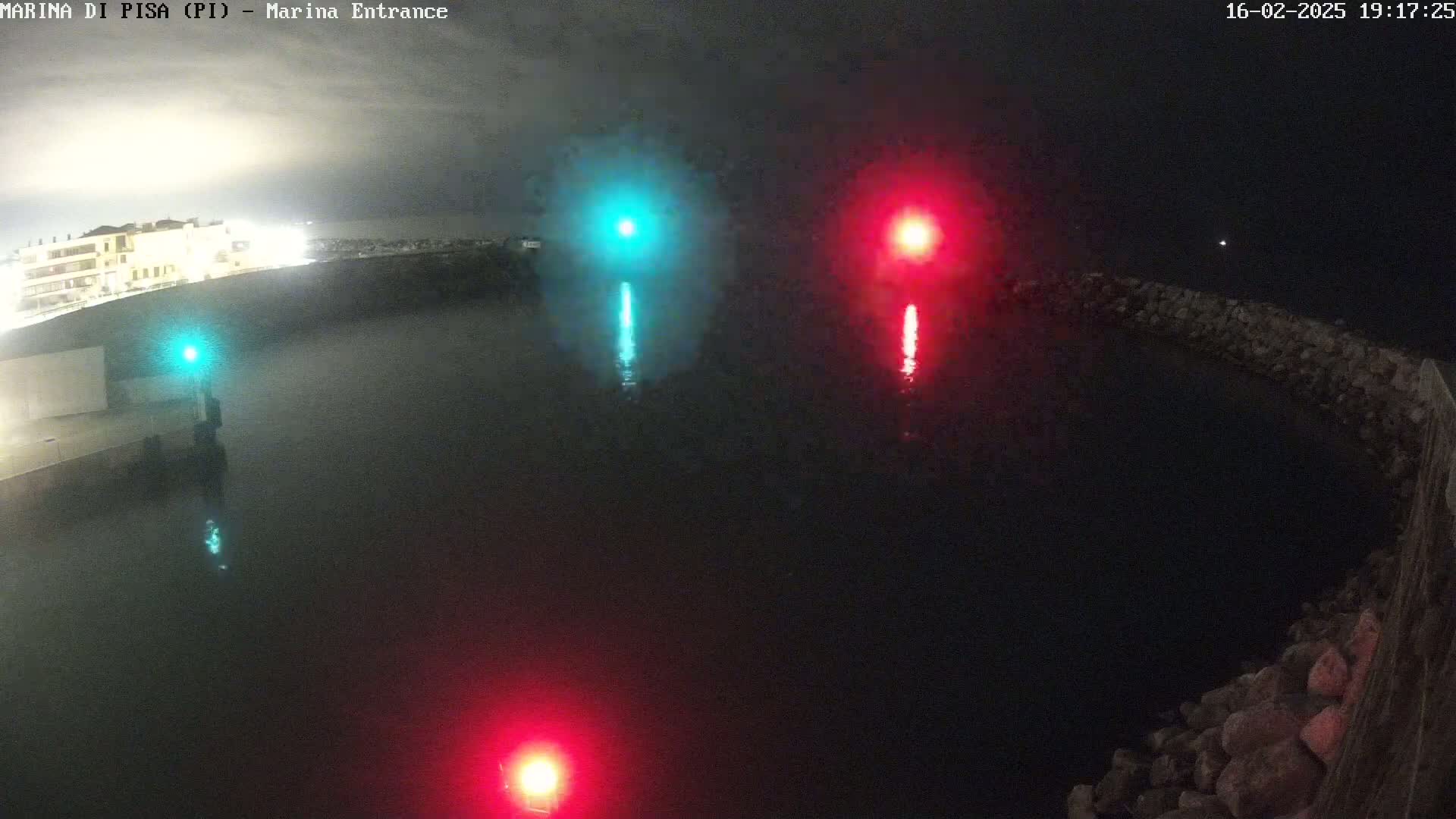 A nighttime, dark view of a harbor entrance with red and green navigation lights reflecting in the calm water.