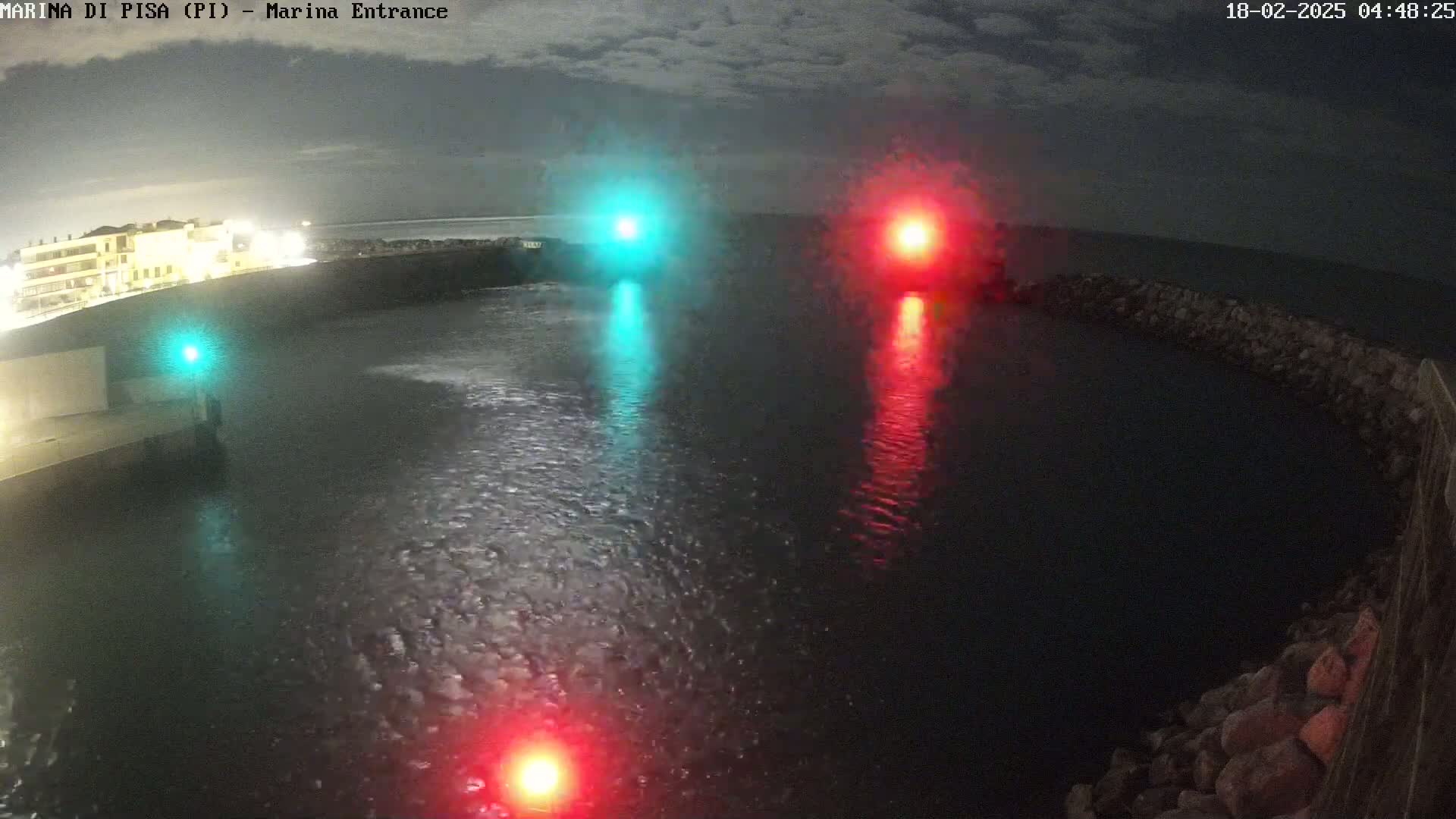 A nighttime view of a harbor entrance with calm water, illuminated by a green and red light on either side of the channel.