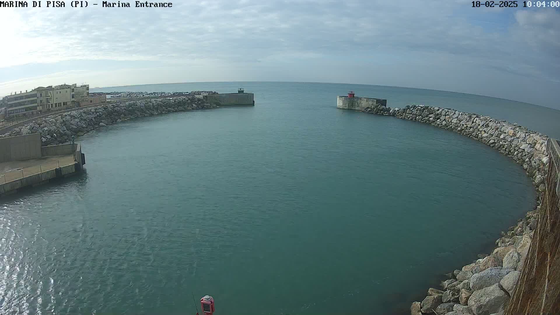 A calm, teal-colored harbor is nestled between two rocky breakwaters under a mostly cloudy sky.
