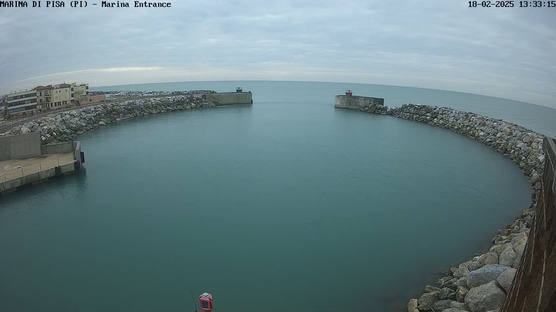 A harbor entrance with calm, teal water is partially enclosed by stone walls on an overcast day.