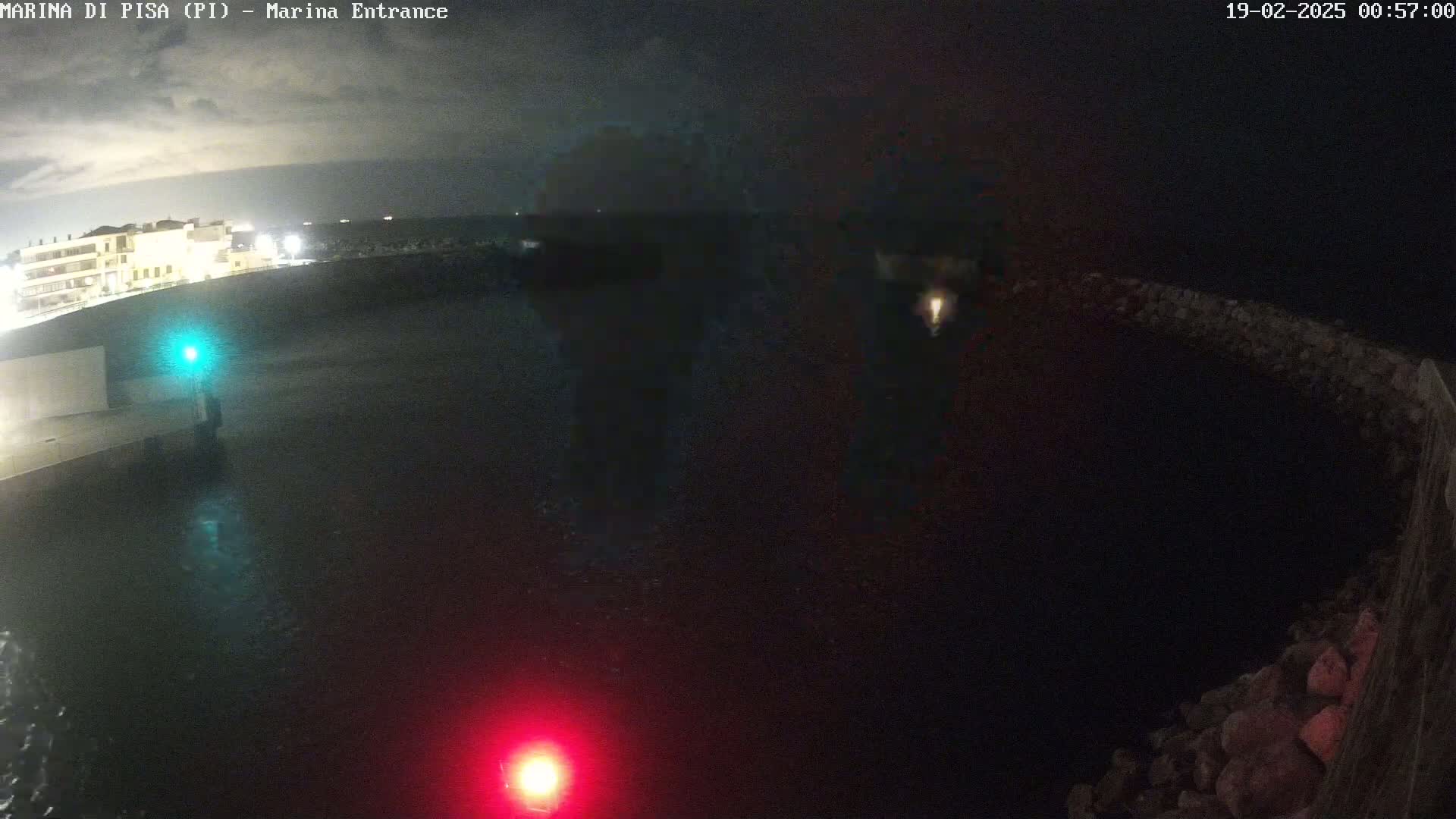 A nighttime view of a dark body of water next to a stone wall, with a building faintly visible in the distance under a cloudy sky.