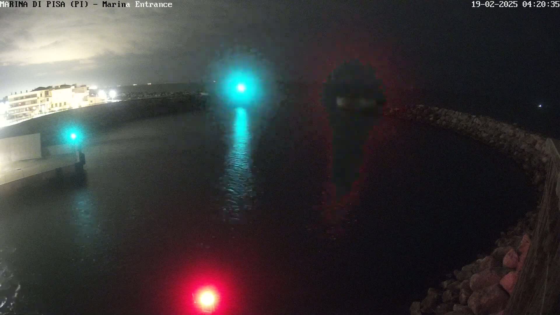 A nighttime view of a dark, rain-slicked harbor with a building and lights visible in the distance.