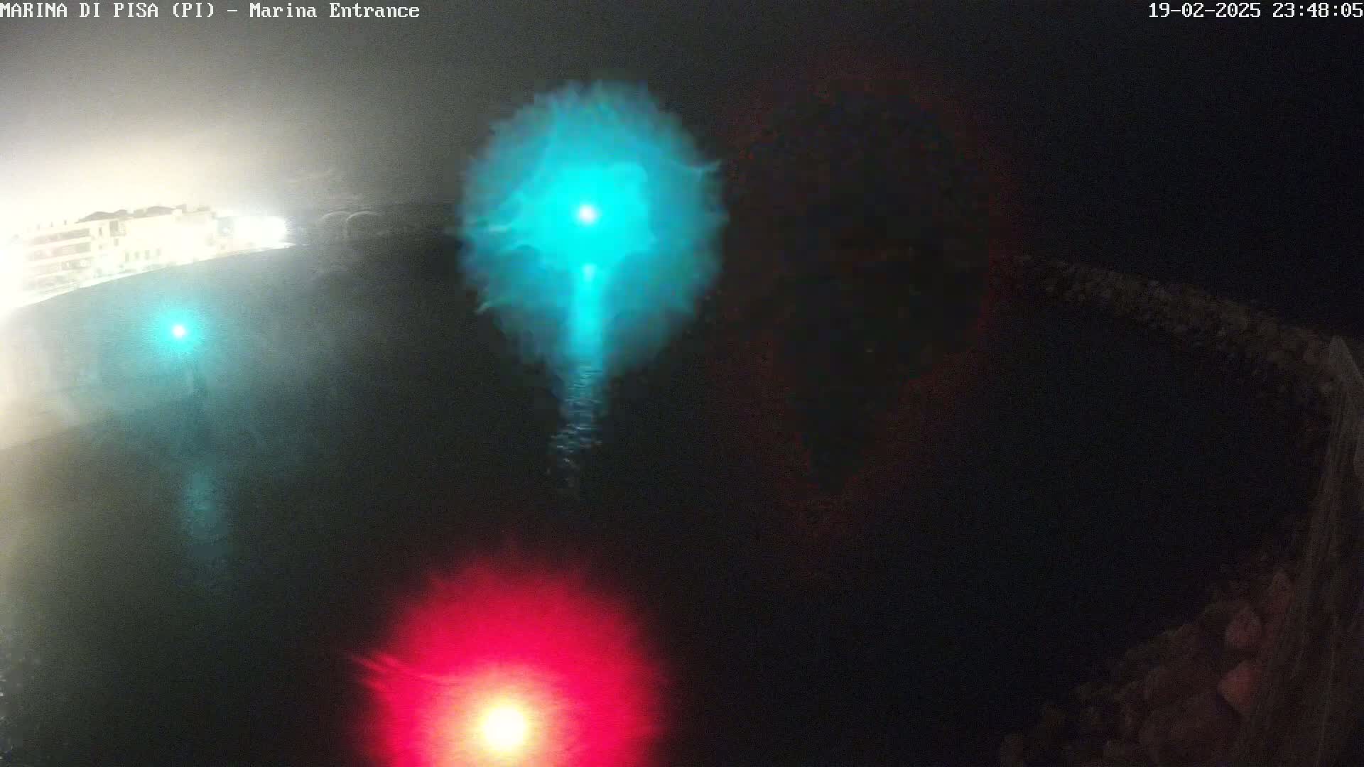 At night, a dark body of water is illuminated by a bright teal light and a red light.