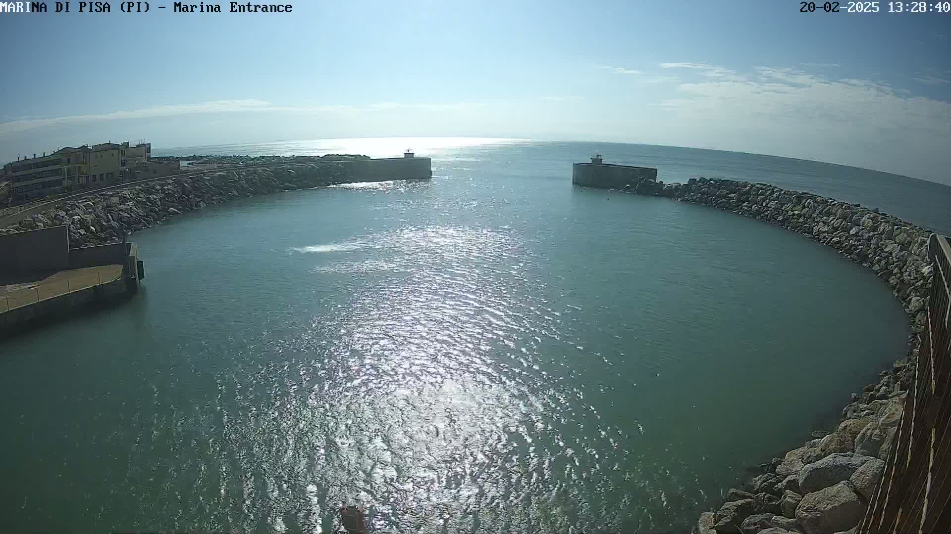 A sunny day reveals a harbor entrance with calm, glistening water surrounded by rock walls and a building in the background.