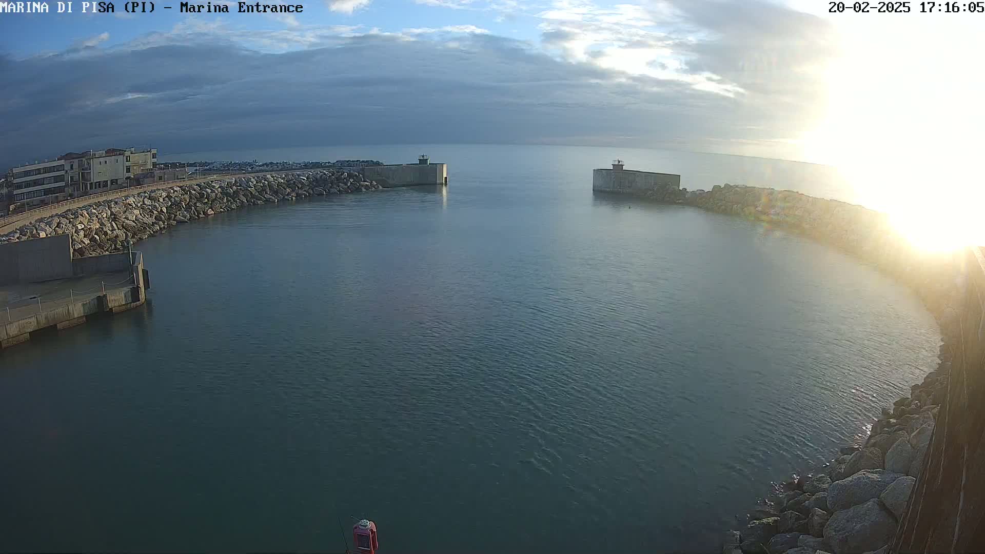 A harbor entrance with calm water under a partly cloudy sky, sunlit from the right.
