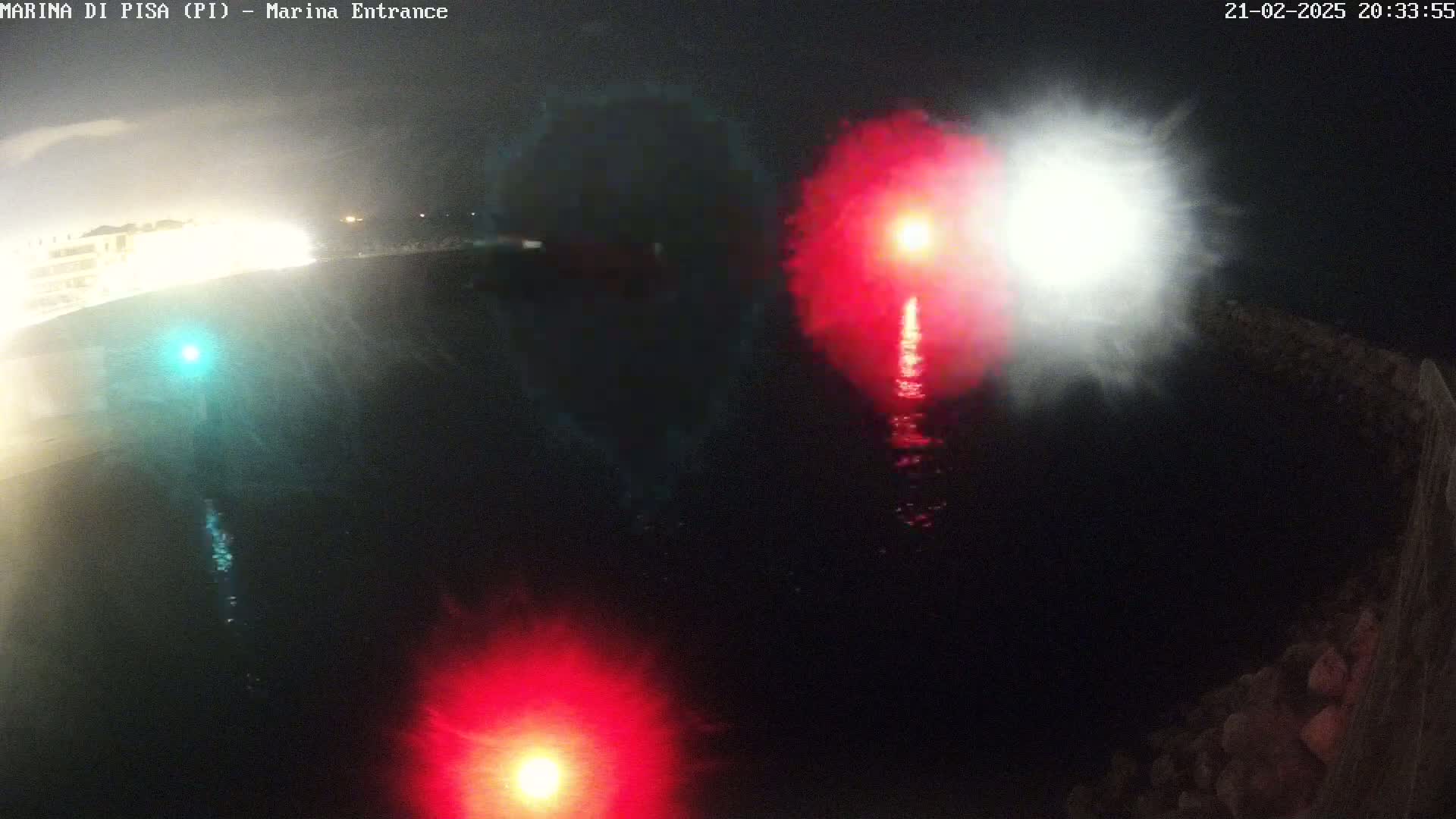 At night, bright red and white lights shine over dark water near a shoreline.