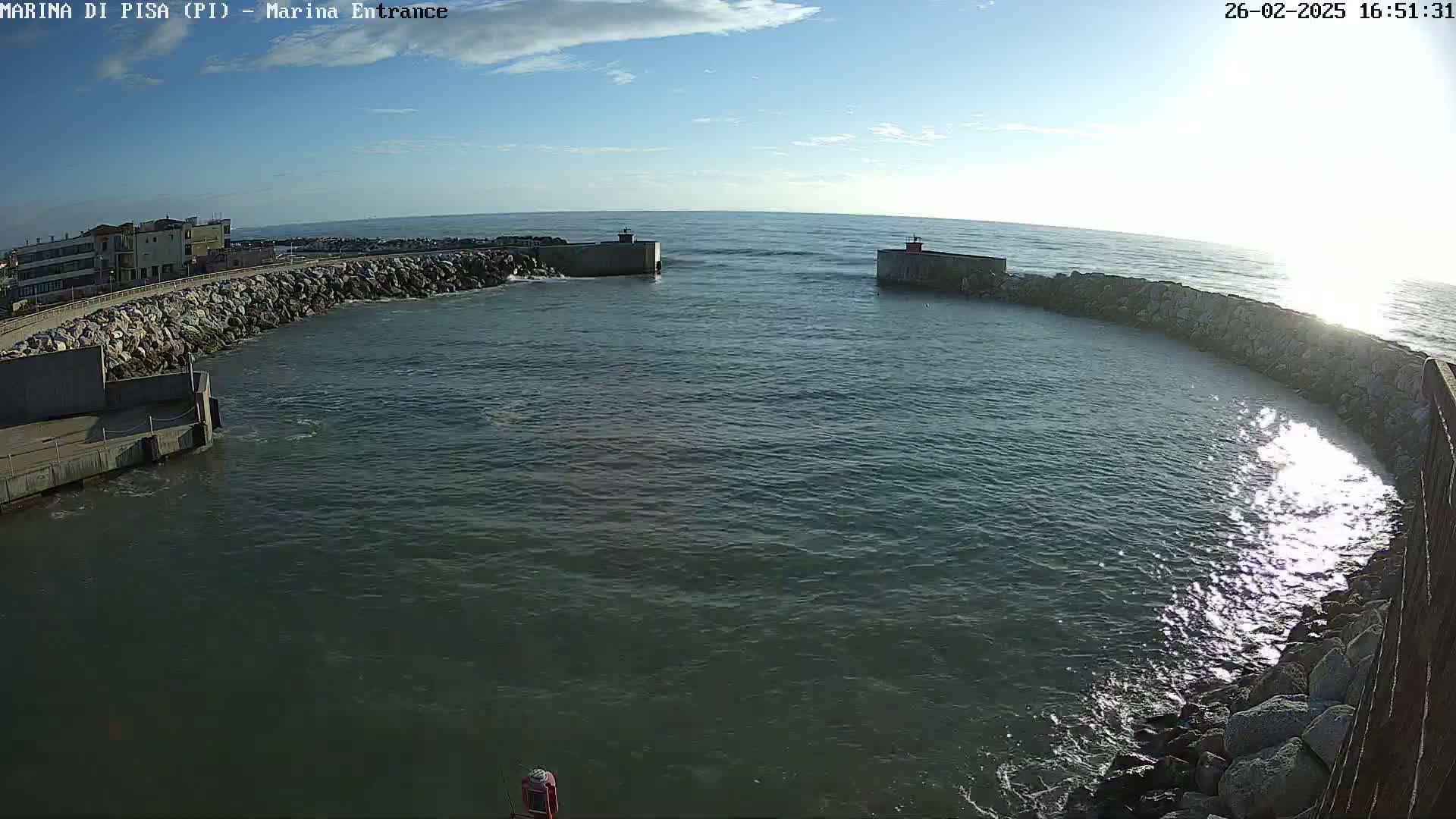 A calm, sunny day reveals a harbor entrance with stone walls and a building visible in the distance.