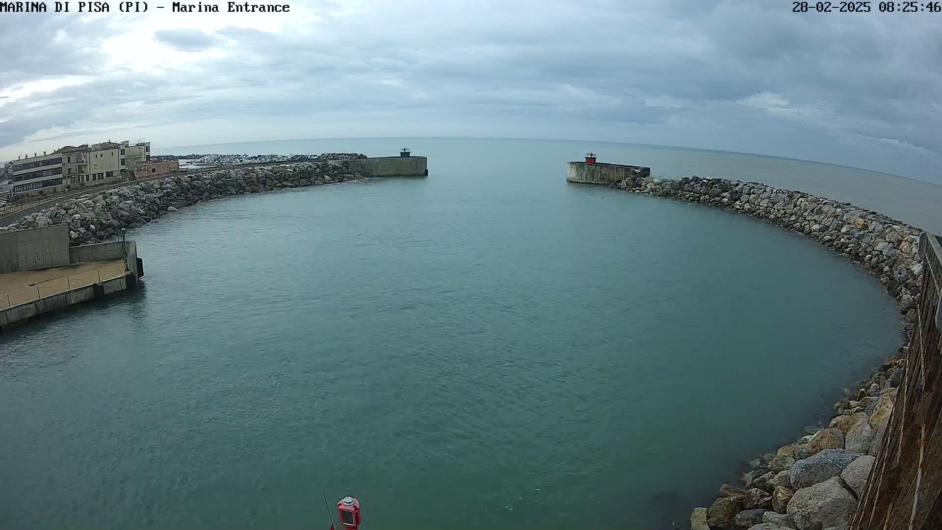 A harbor entrance with calm, dark-green water is partially enclosed by rocky breakwaters under an overcast sky.