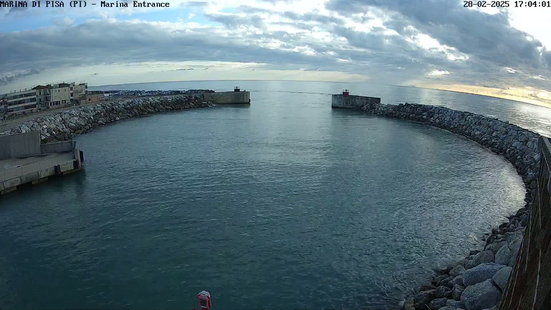 A harbor entrance with calm water under a partly cloudy sky.