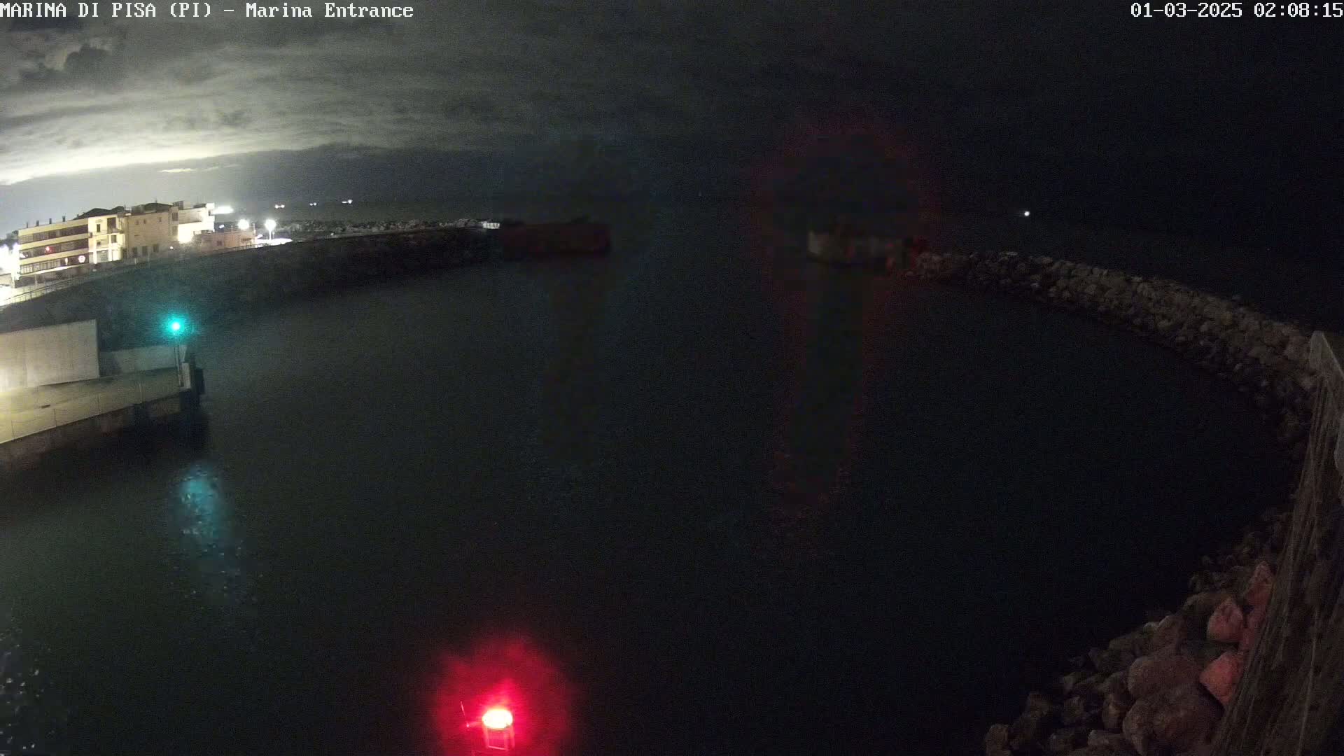 A nighttime view of a dark harbor with a building in the background under a cloudy sky.
