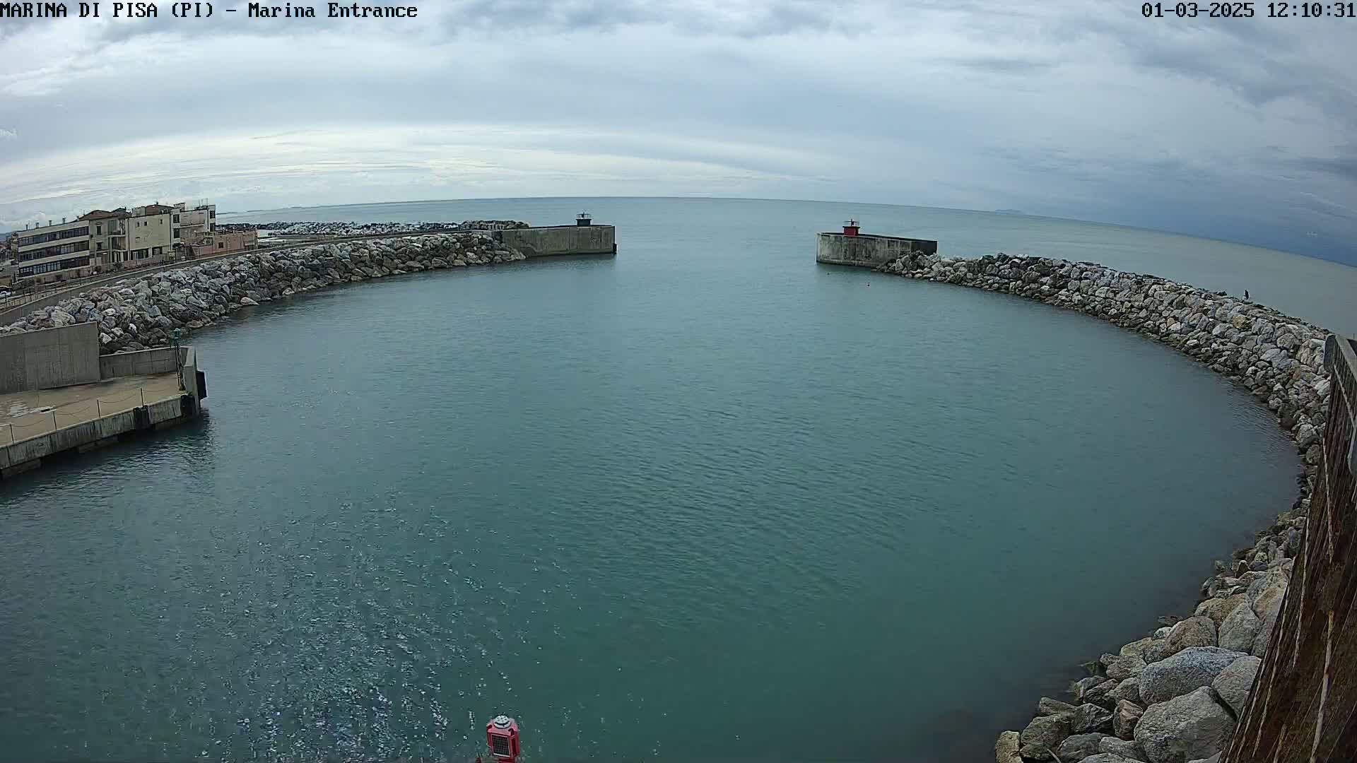 A harbor entrance with calm, teal water is partially enclosed by stone walls under a cloudy sky.