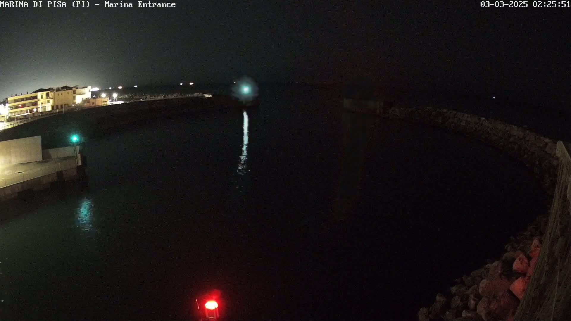 A nighttime view of a dark harbor with a single vessel's lights visible on the water.