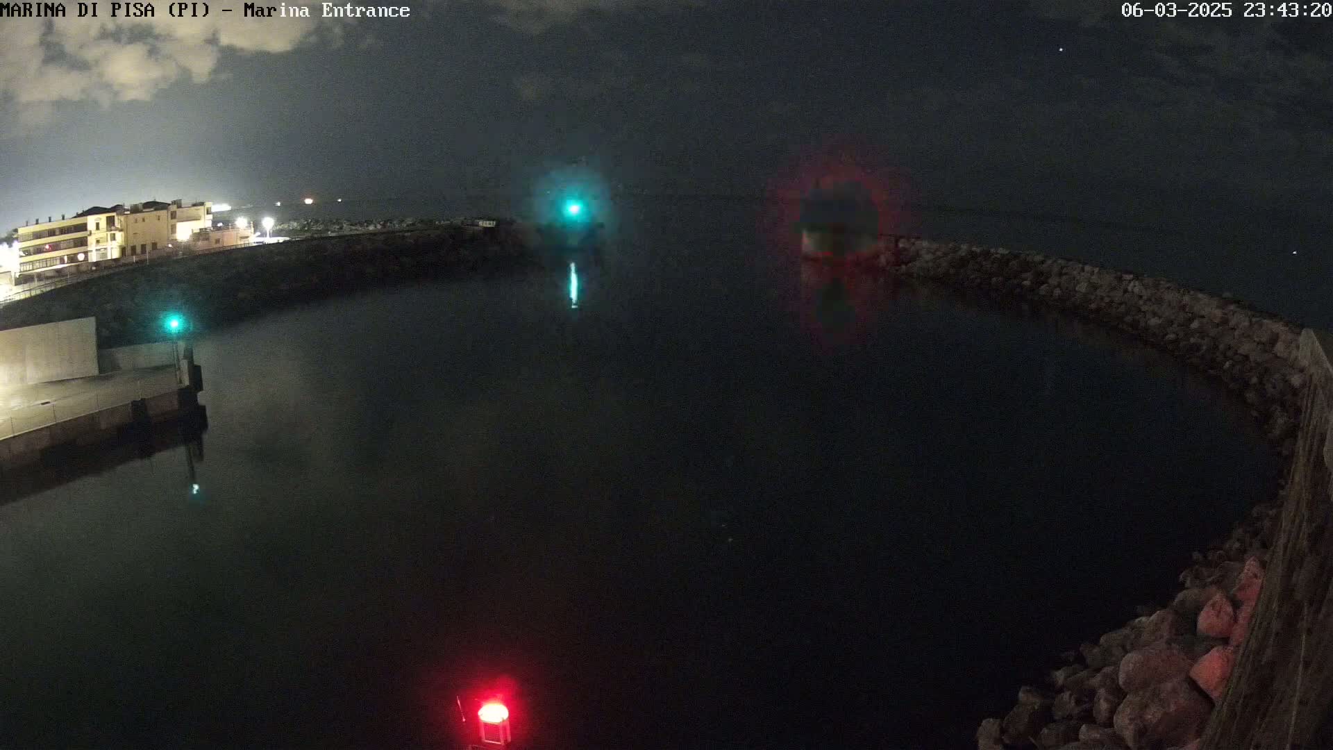 A nighttime view of a dark harbor with a building in the background, partially illuminated by lights, under a cloudy sky.
